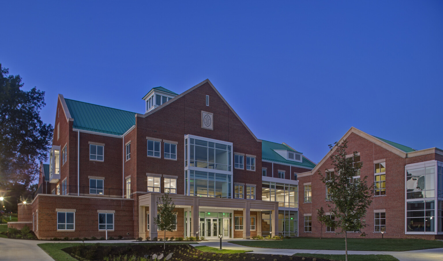 A multistory brick building with green roof and glass wall accents illuminated at night. Brown covered entry at driveway