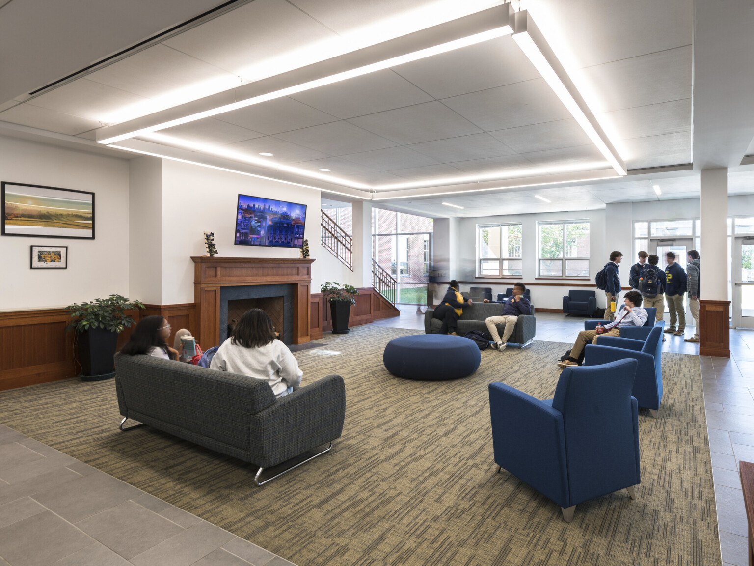 Lobby with wainscotting and fireplace on the wall, seating includes sofas and chairs with glass facing the exterior.