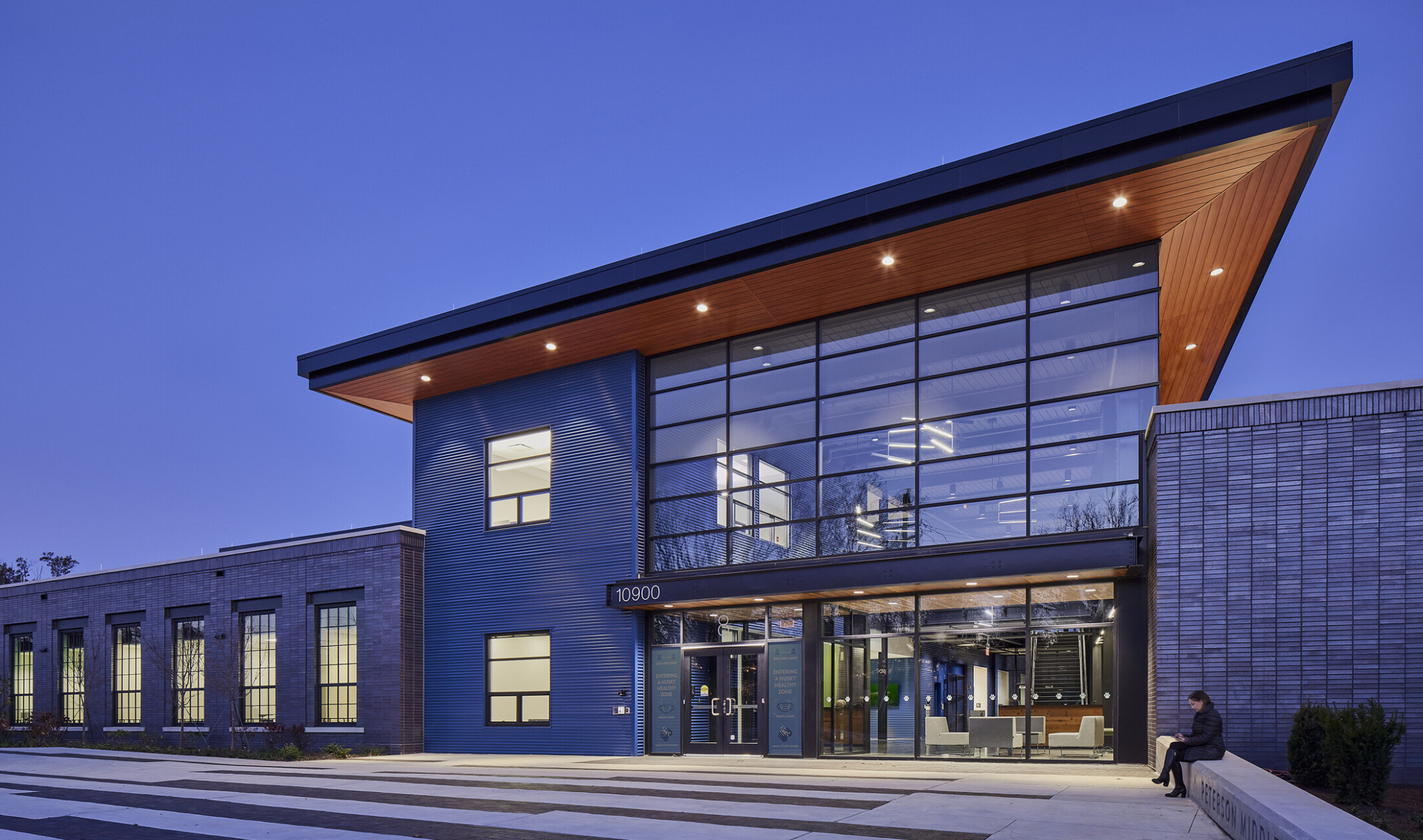 exterior of a doubleheight modern architecture glass atrium with a wood canopy overhang at Peterson Middle School