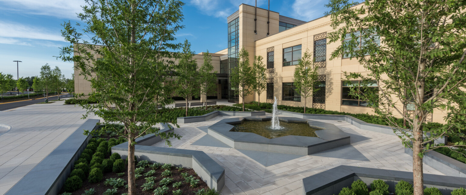 exterior view of campus complex, precast concrete exterior façade, Arabic architectural patterns, trees, landscaping, concrete pathways, in the center, an eight-point star shaped water feature