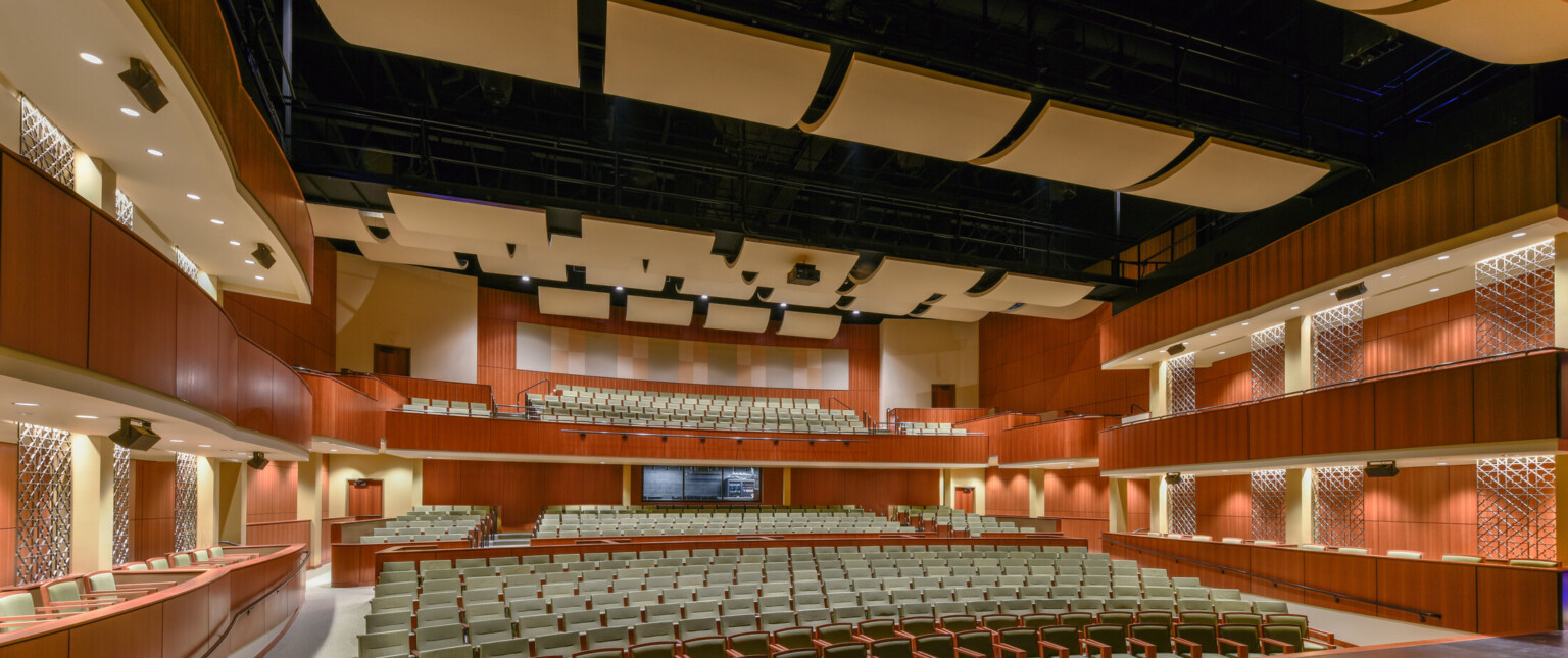 550-seat performing arts theater, view from stage, ceiling-suspended sound baffling, stage lights, opera boxes, warm wood paneling on walls and seating