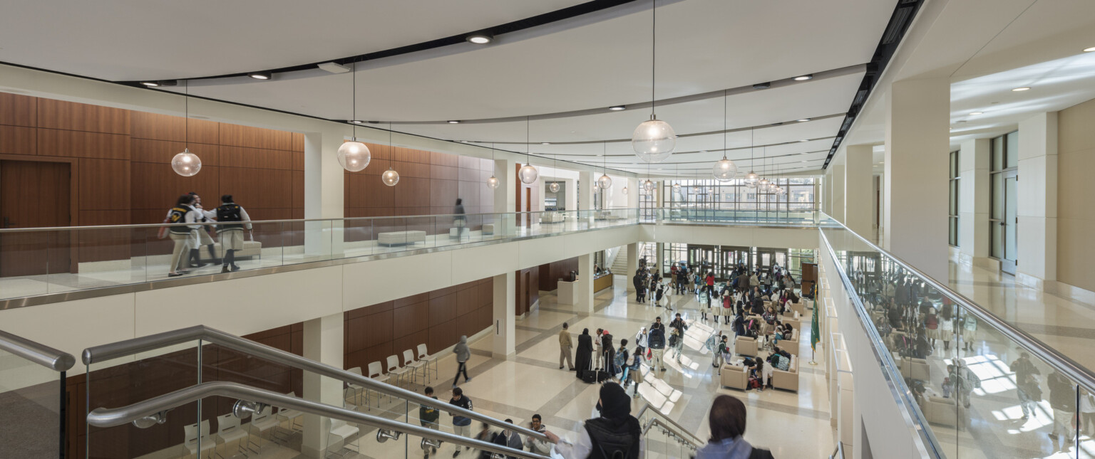 central atrium at a school with a large stair connecting the upper and lower floors, wood panel walls and white hallways