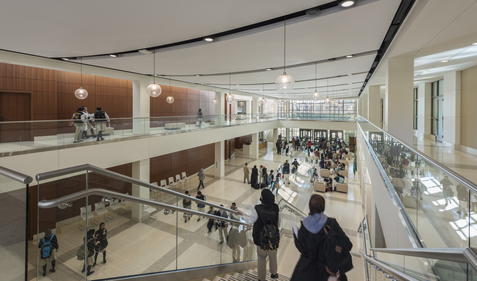 central atrium at a school with a large stair connecting the upper and lower floors, wood panel walls and white hallways