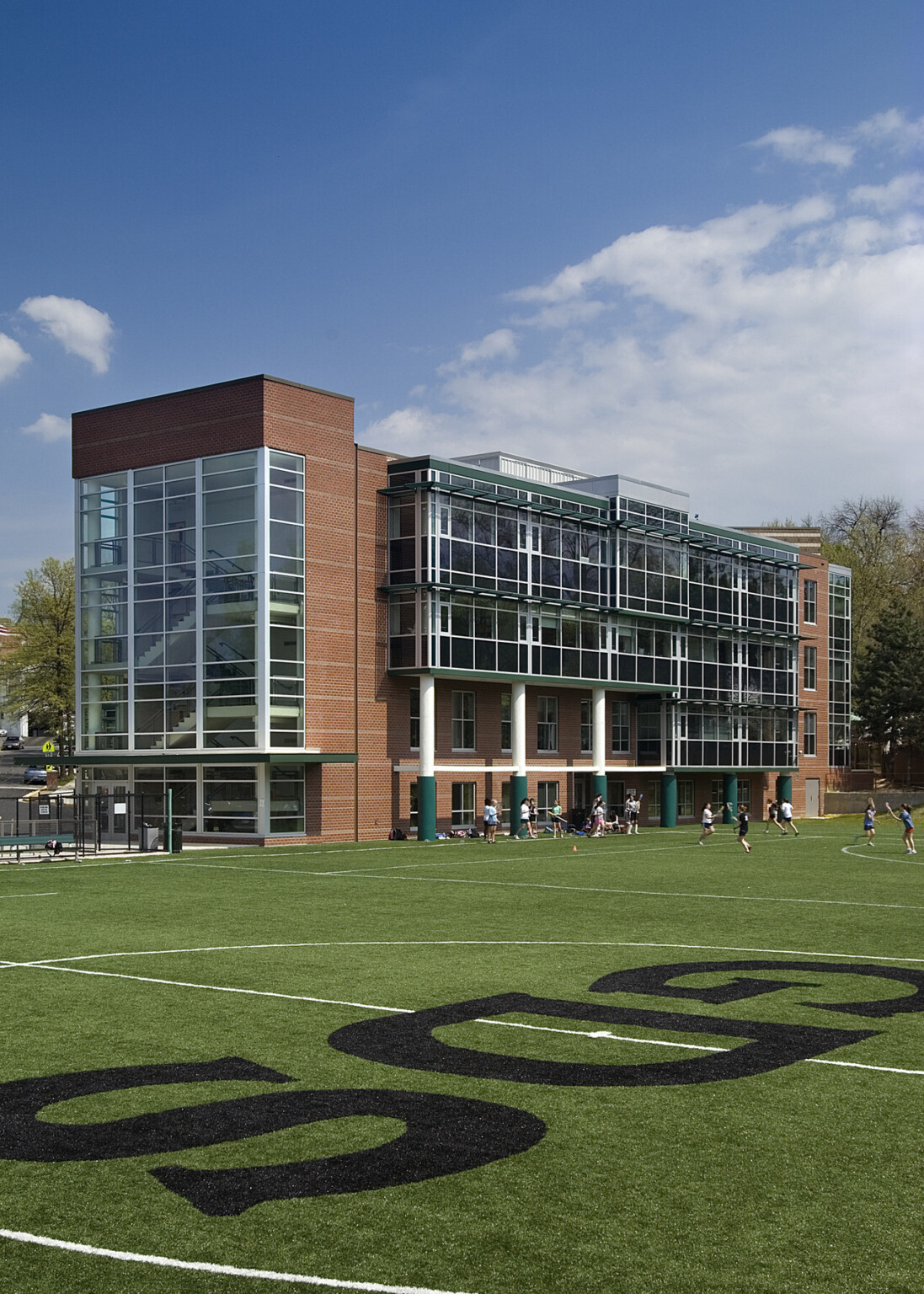 Multistory brick building with green accents and lots of glass windows behind a lush green playing field