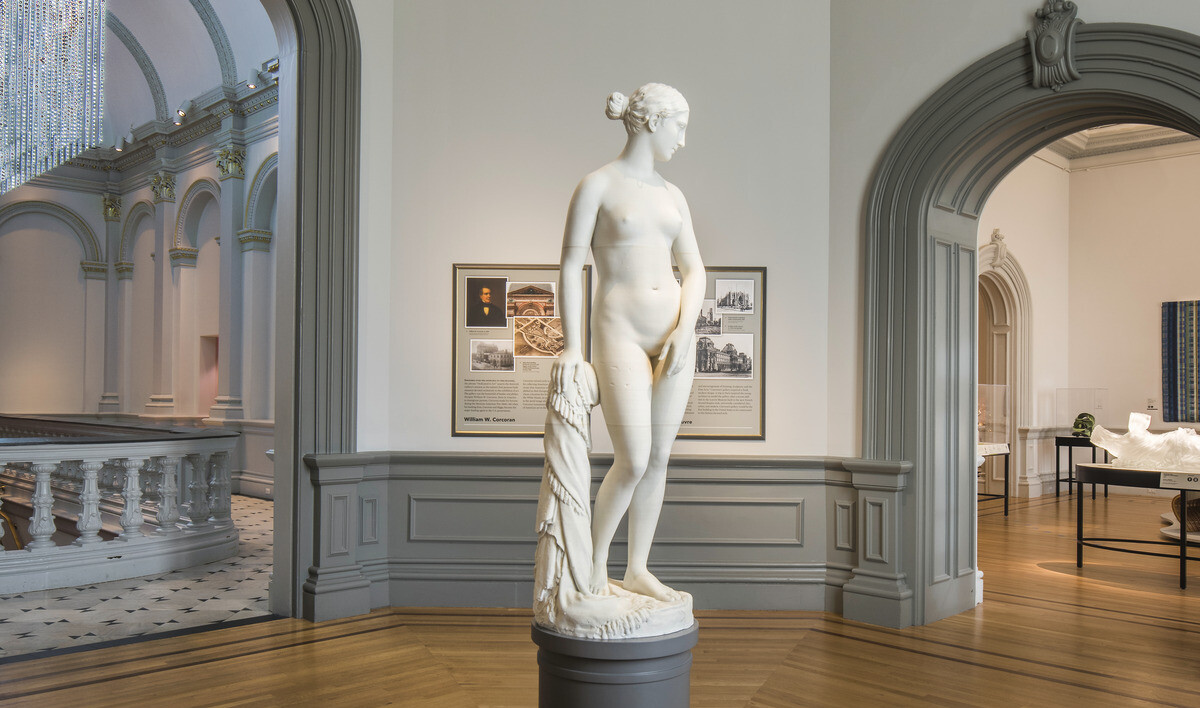 Sculpture of a woman stands on a podium in the center of rotunda with arching molded grey doors. Crown molding above