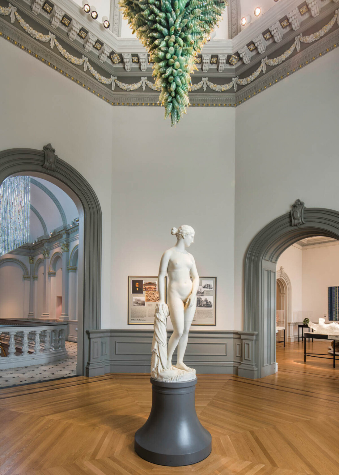 Sculpture of a woman stands on a podium in the center of rotunda with arching molded grey doors. Crown molding above