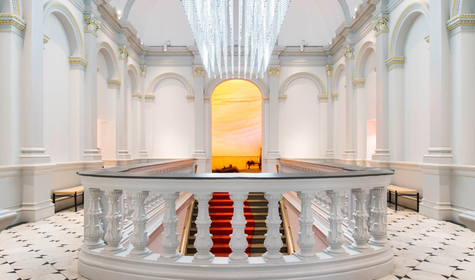 Custom sculptural chandelier hanging parallel above staircase in white room, banister with dark accent in front