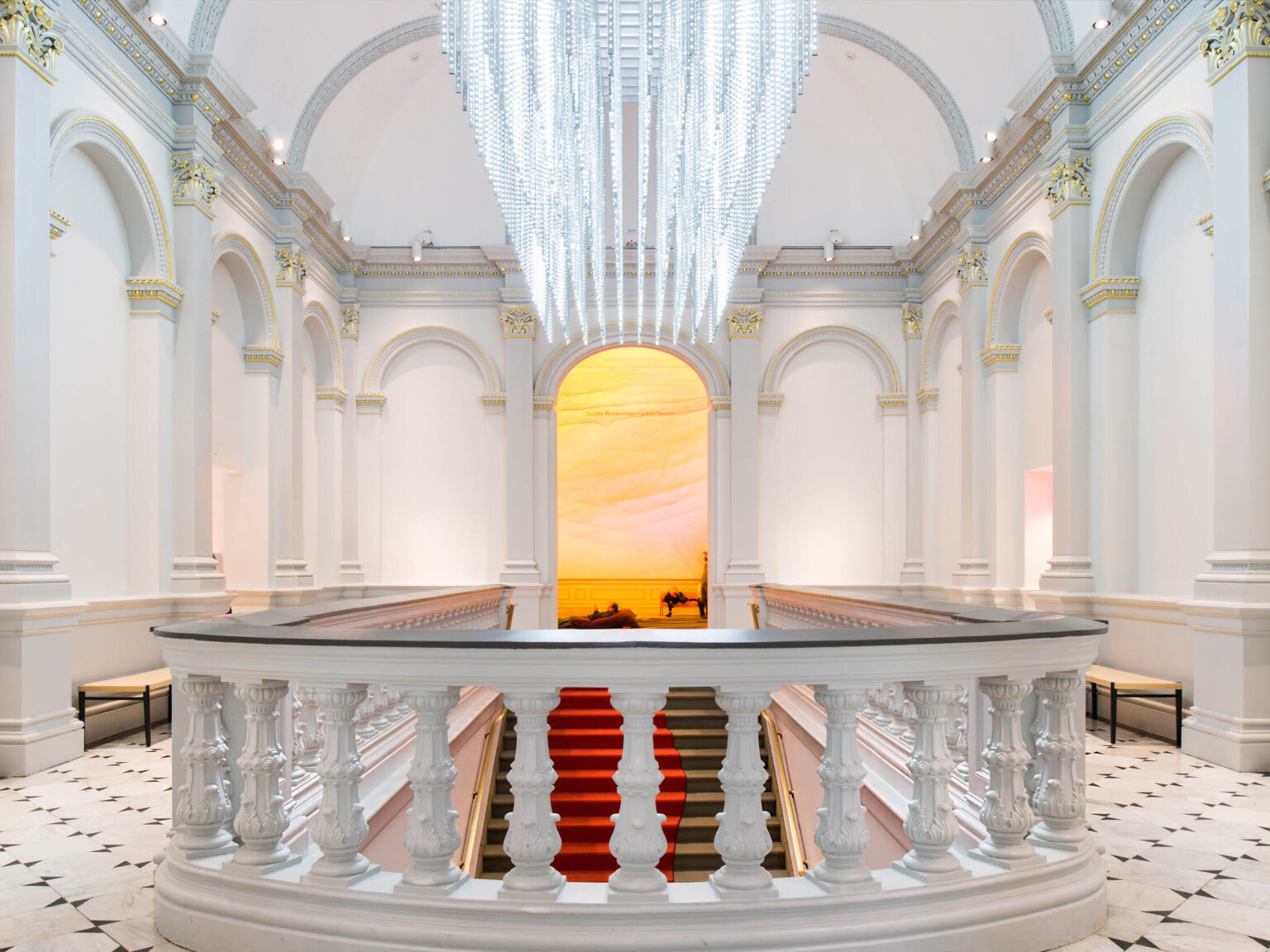 Custom sculptural chandelier hanging parallel above staircase in white room, banister with dark accent in front