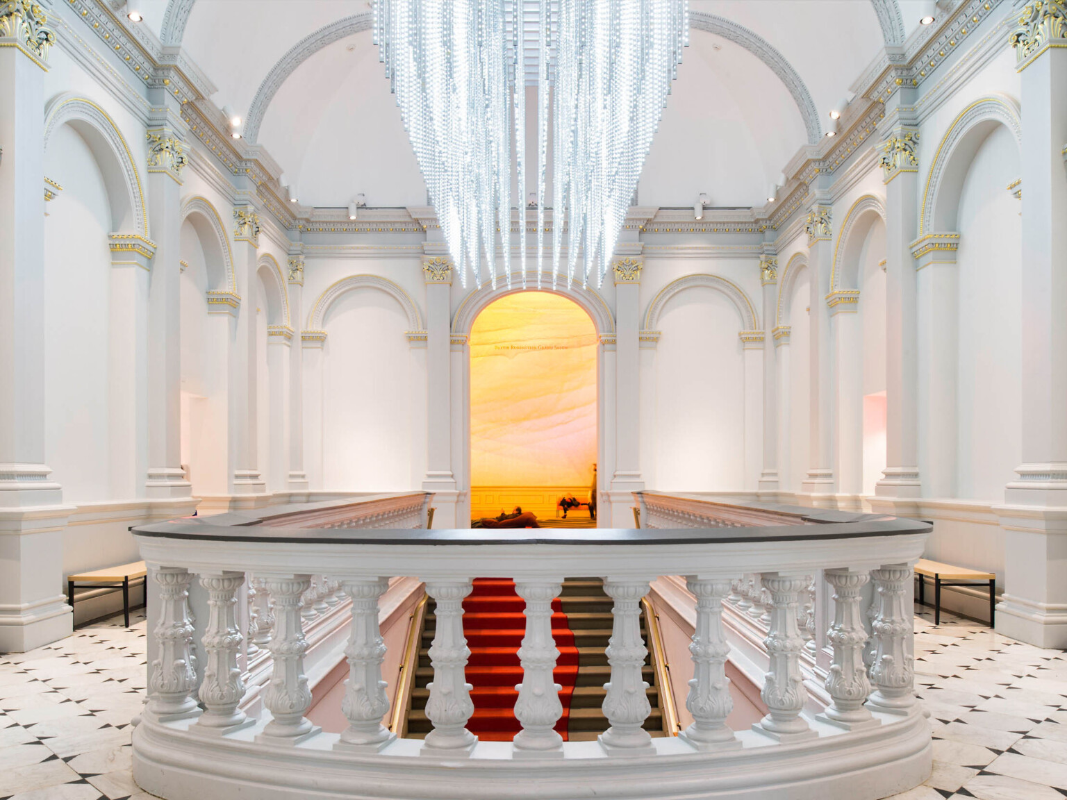 Custom sculptural chandelier hanging parallel above staircase in white room, banister with dark accent in front