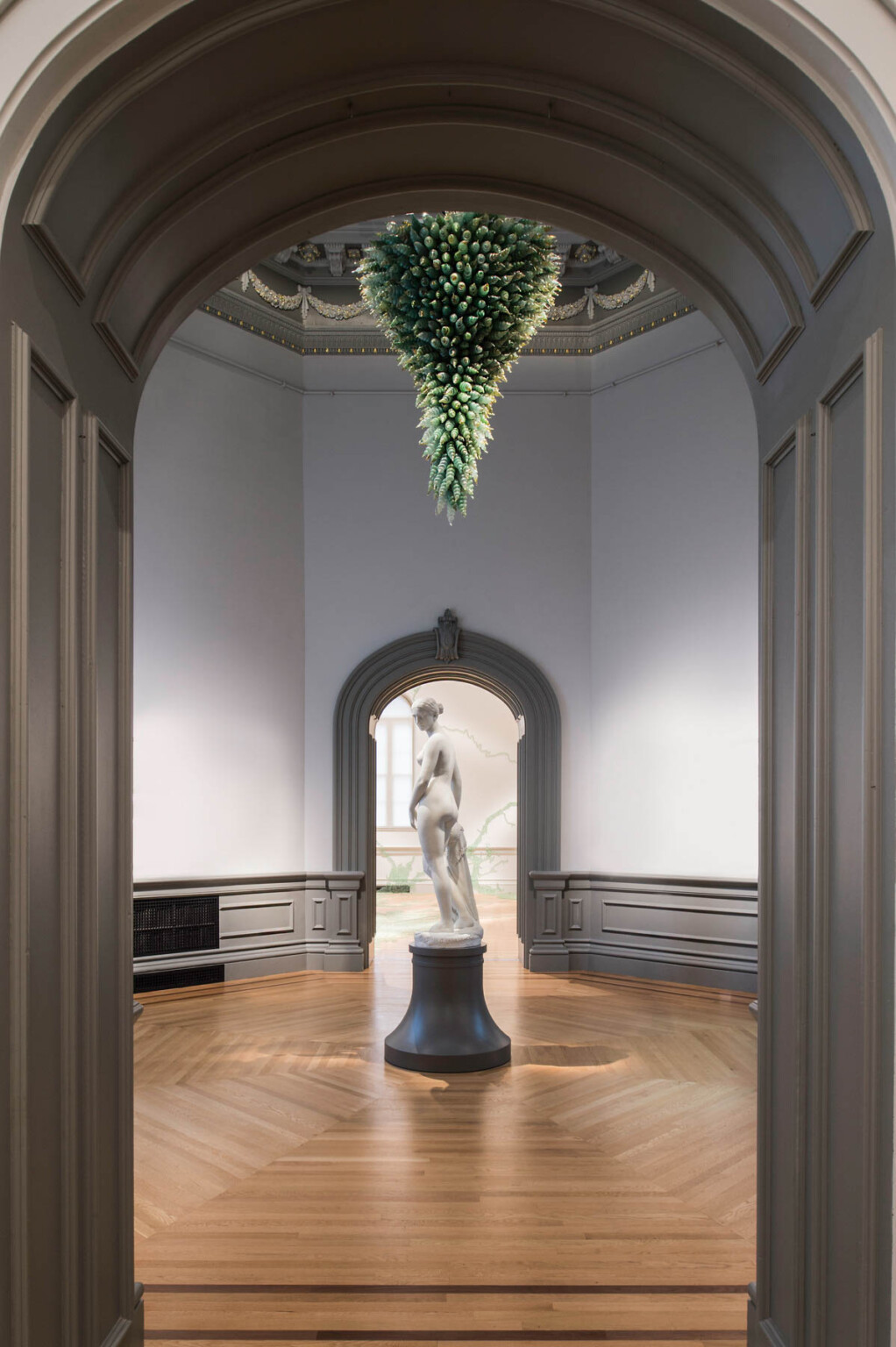 Marble sculpture of a woman on a black pedestal in the center of a small room, framed in front and behind by molded door frame