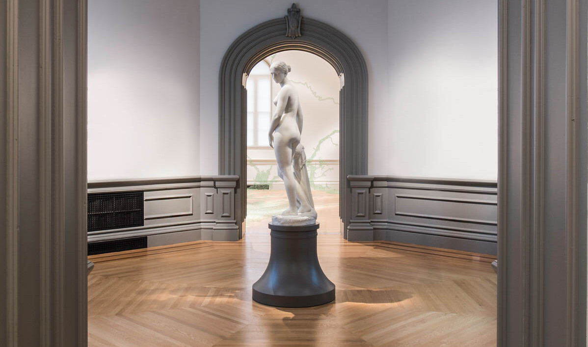 Marble sculpture of a woman on a black pedestal in the center of a small room, framed in front and behind by molded door frame