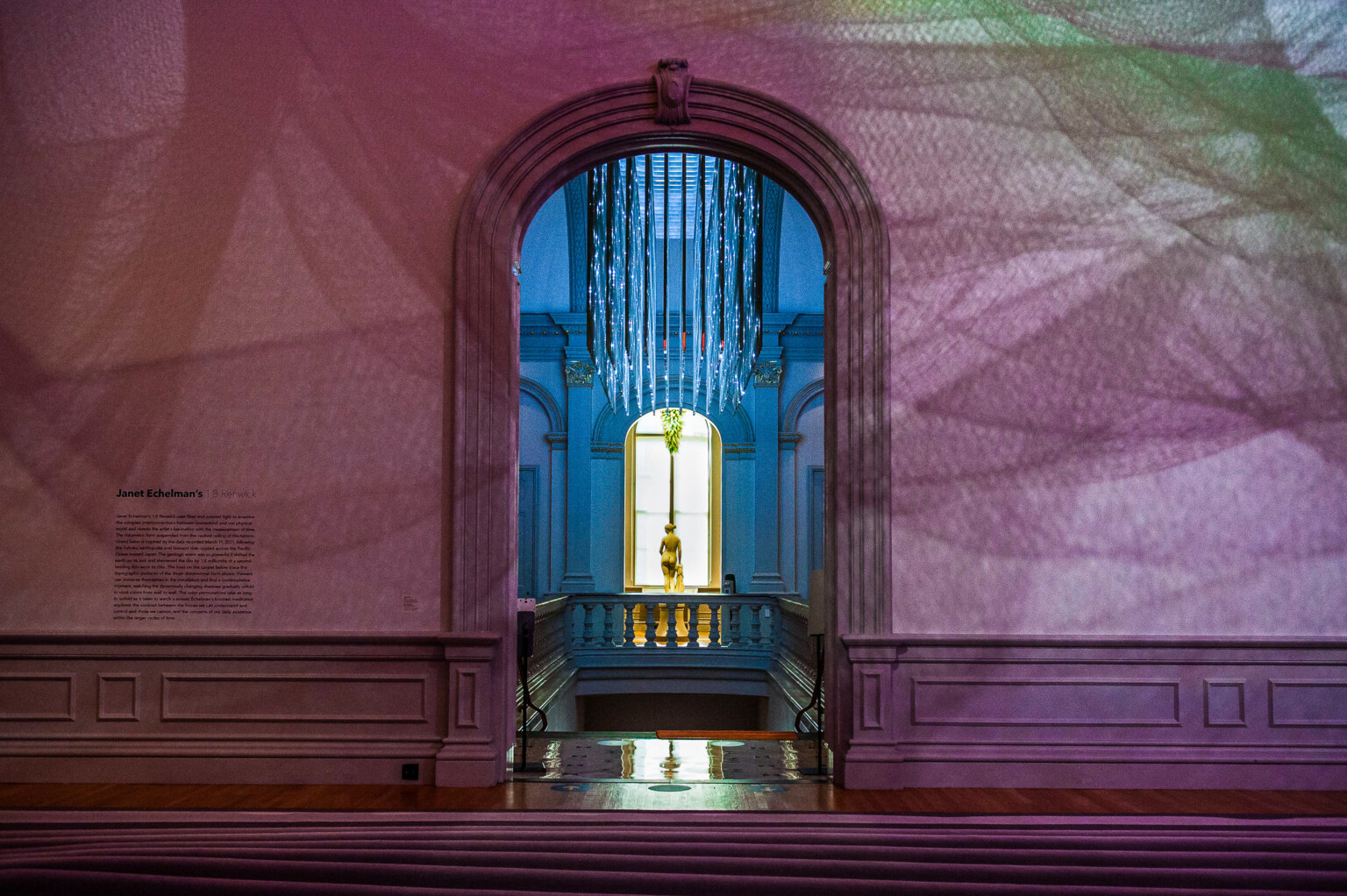 Arched doorway framing a statue lit by natural light, with patterned shadows on classical walls.