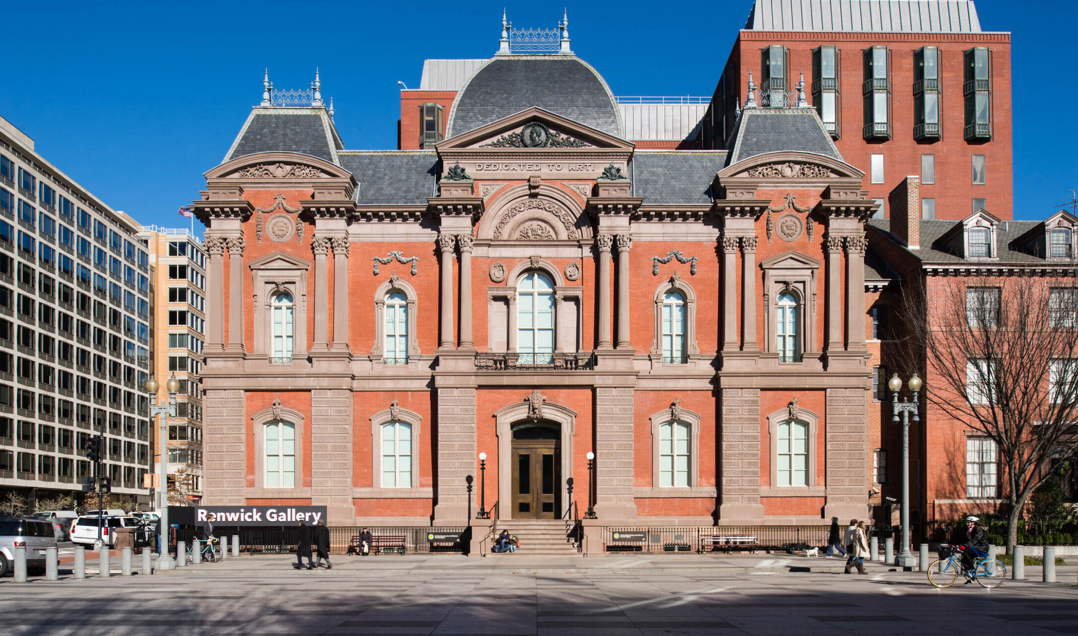 The front entrance to a two story red brick Second Empire style building with masonry and Dedicated to Art is carved at top