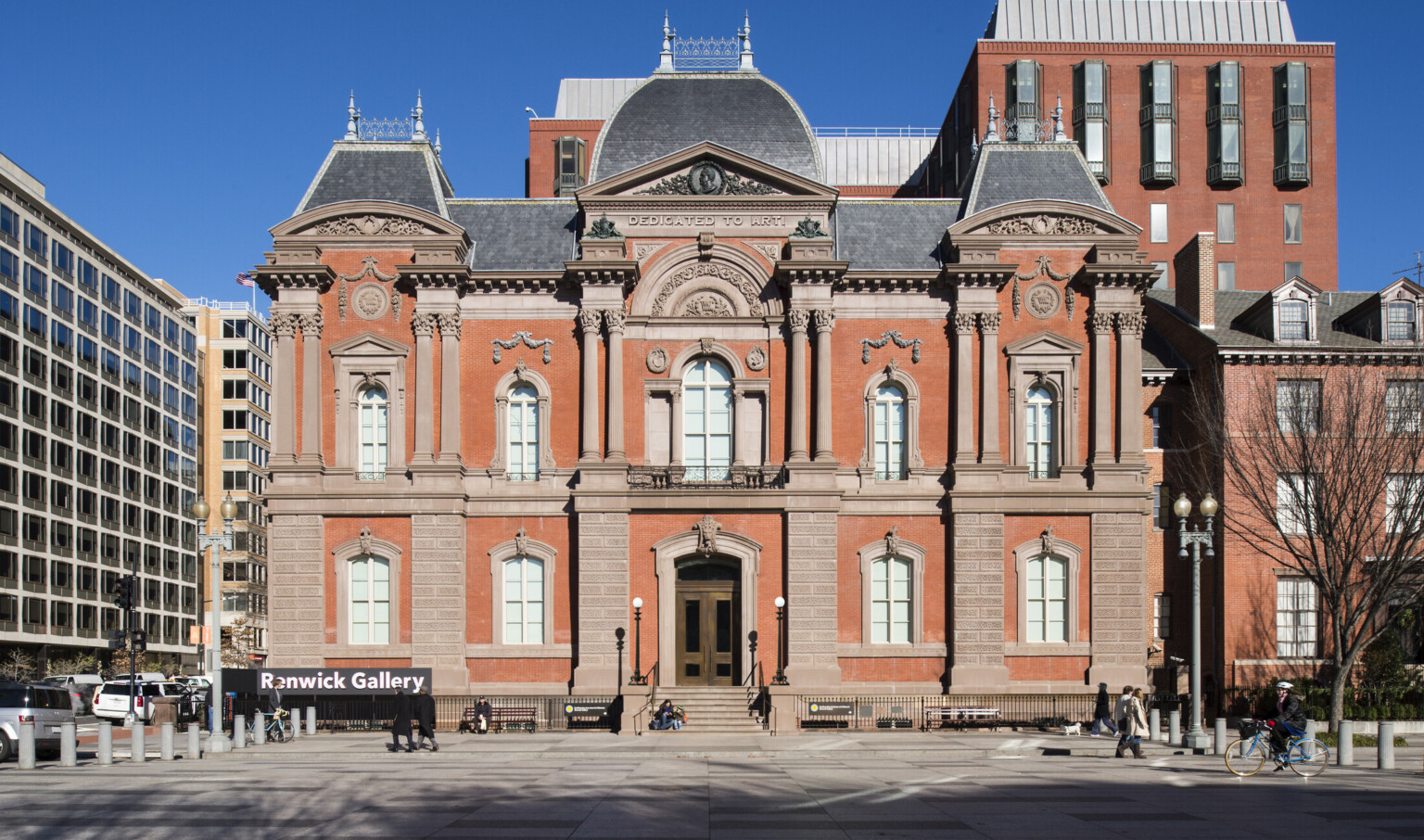 The front entrance to a two story red brick Second Empire style building with masonry and Dedicated to Art is carved at top