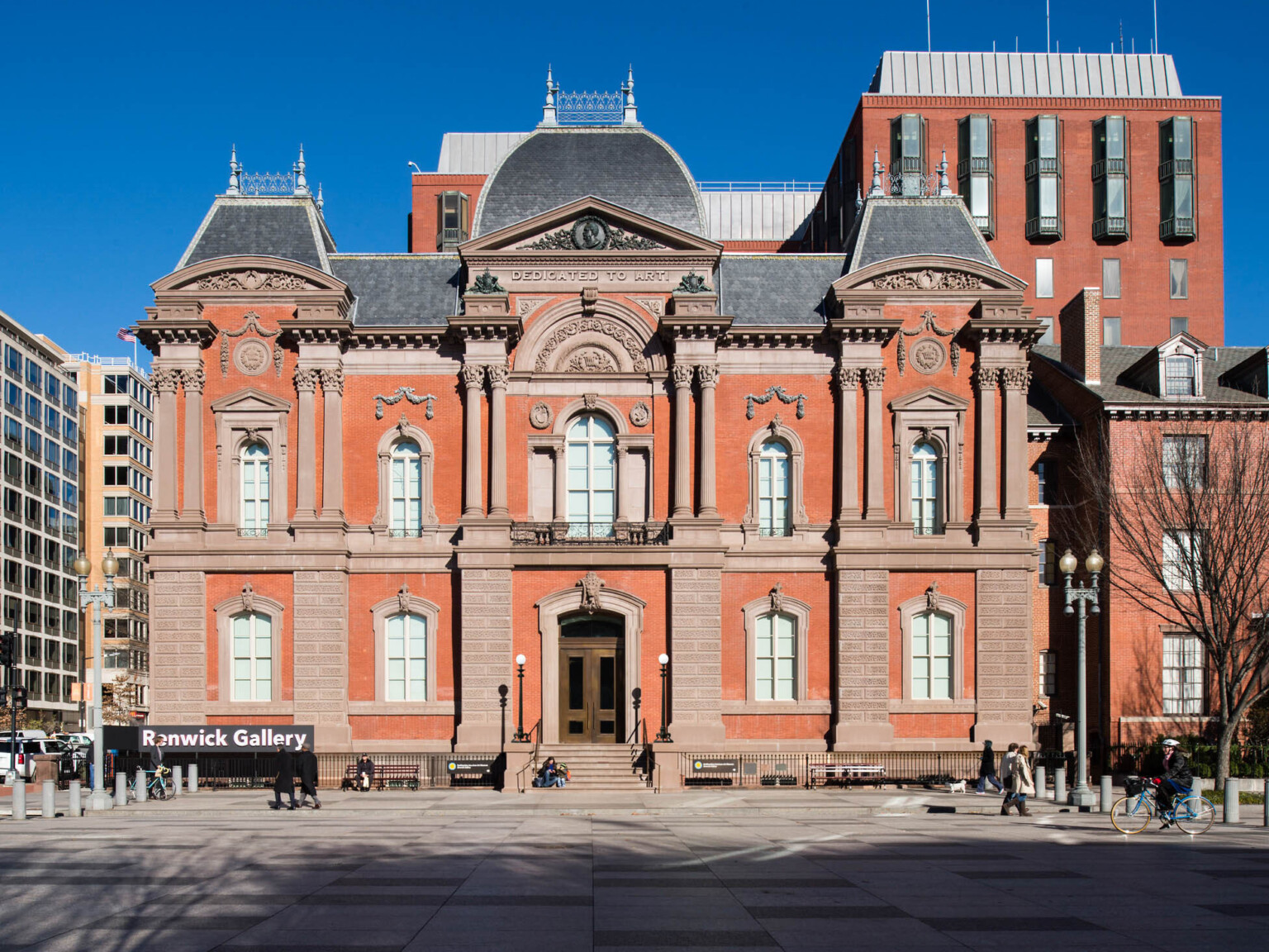 The front entrance to a two story red brick Second Empire style building with masonry and Dedicated to Art is carved at top