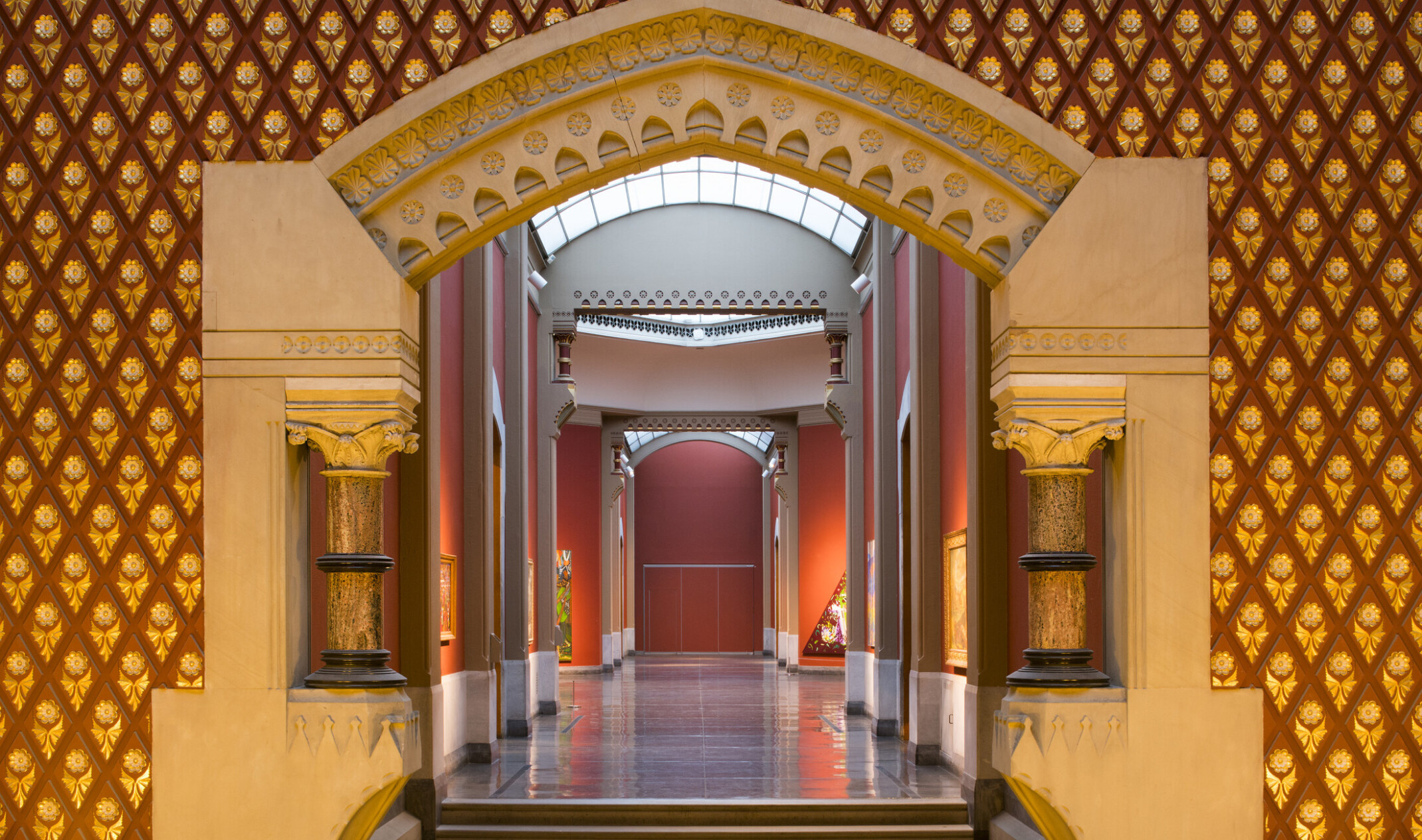Corridor entry with sculpted stone archway with banded Corinthian columns. The hall is painted red with skylights above