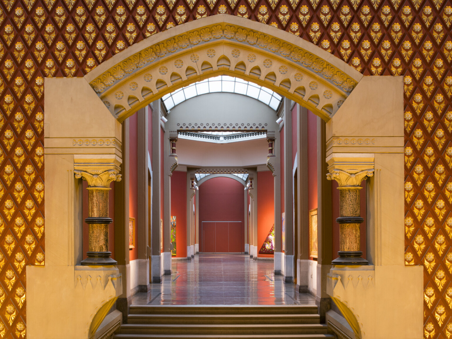Corridor entry with sculpted stone archway with banded Corinthian columns, the hall is painted red with skylights above
