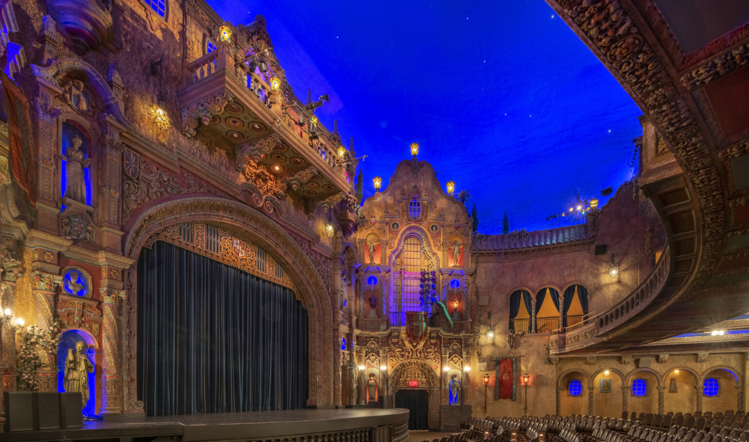 View looking to stage with ornate proscenium and audience chamber modeled after a Mediterranean courtyard with blue and orange lights