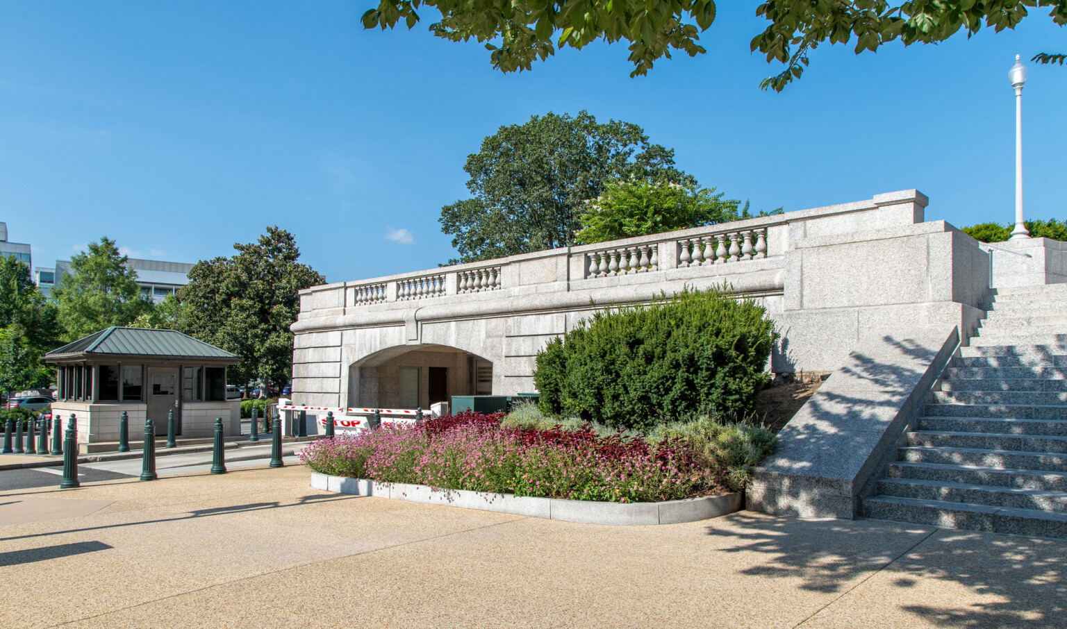 An alternative entrance to the under ground garage features natural landscaping, stairs, an upper walkable bridge that sits over the vehicle entrance, and a small booth