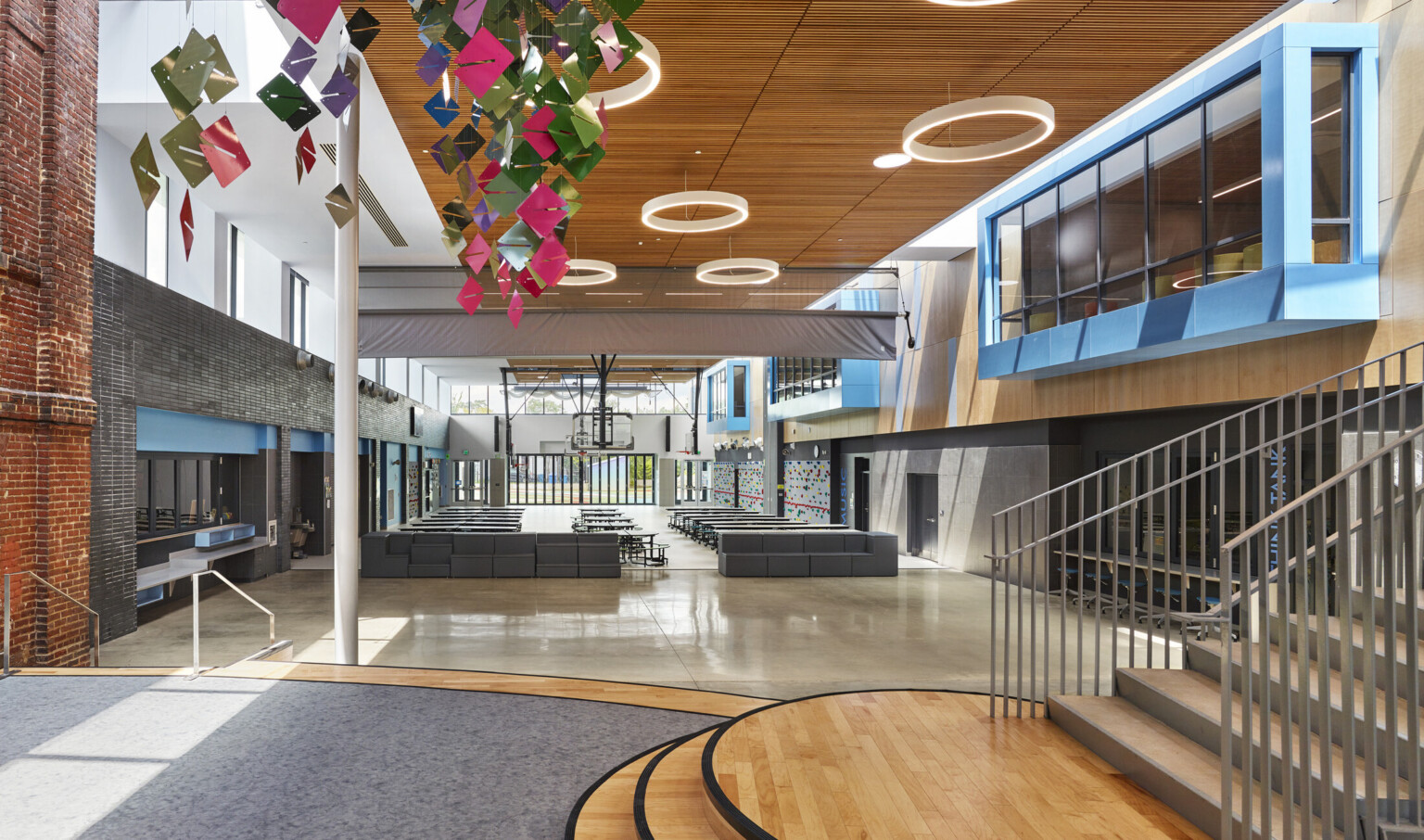 Double height atrium with exposed brick, left, and blue overhanging 2nd floor windows, right. Multicolor sculpture hangs left