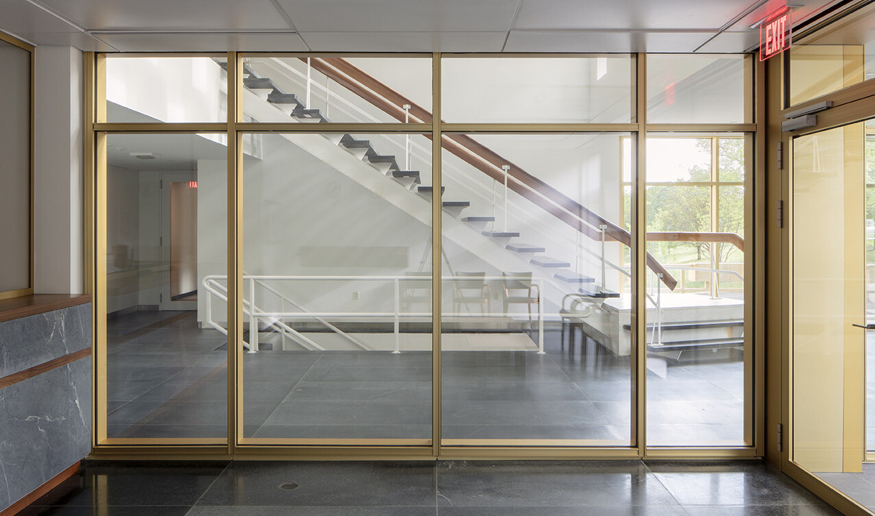 Interior hallway with glass wall looking to floating stairs to upper level, exterior windows connect to nature