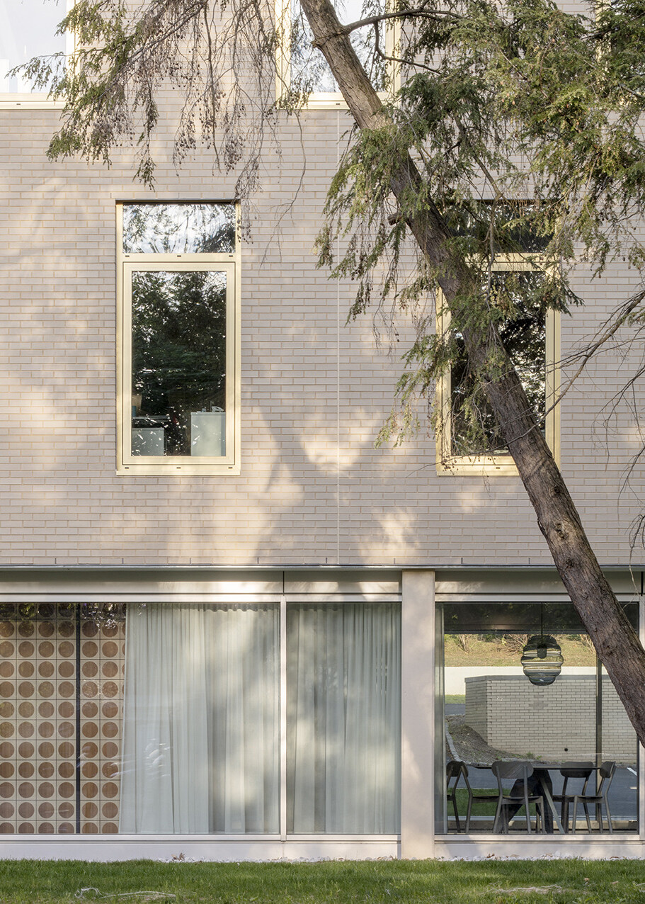Exterior wall of grey stone midcentury building, floor to ceiling windows on ground level, curtains