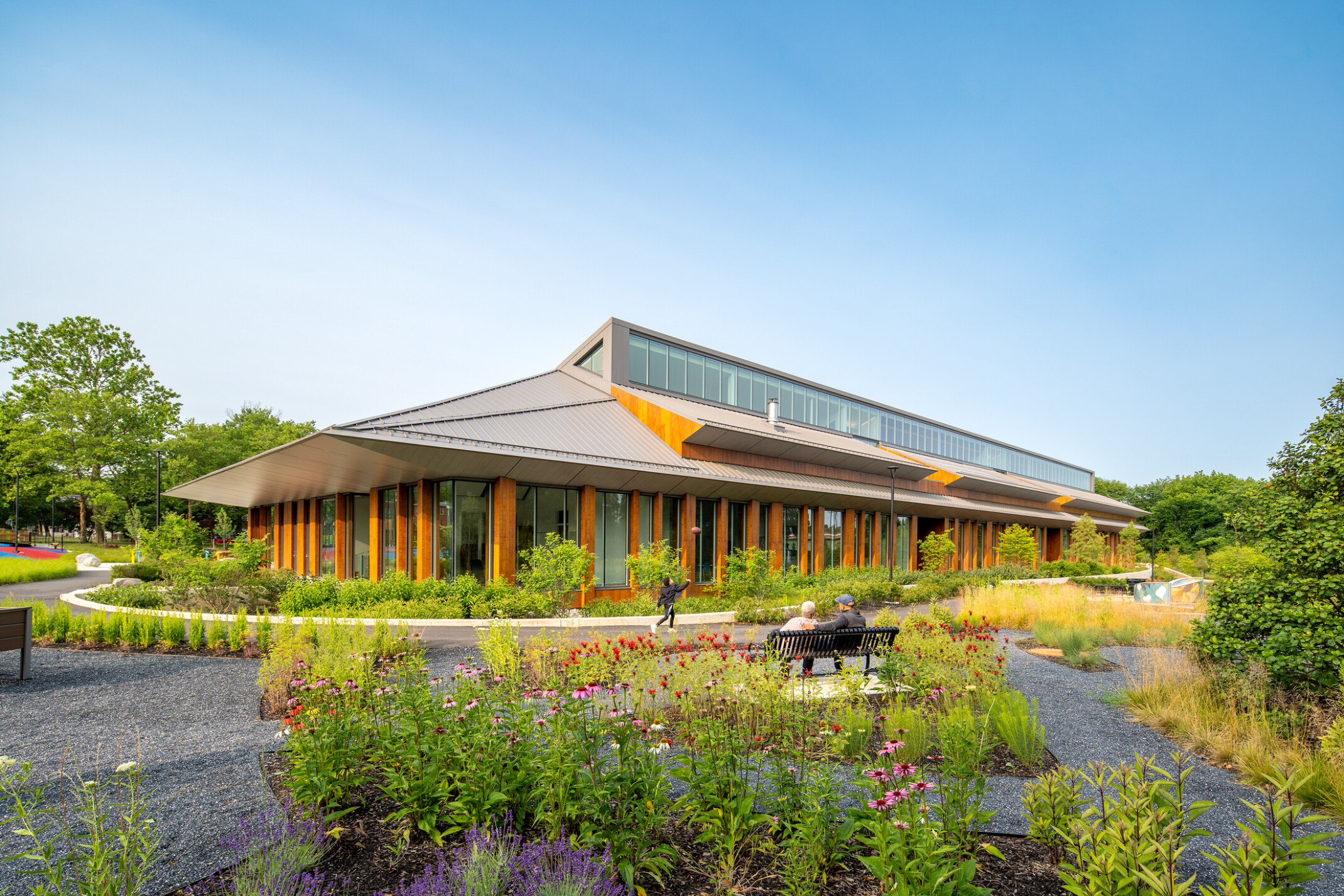 Joy Evans Therapeutic recreation center building; exterior photo with lots of greenspace and pathways to the wood and grey building; pointed roof with large windows