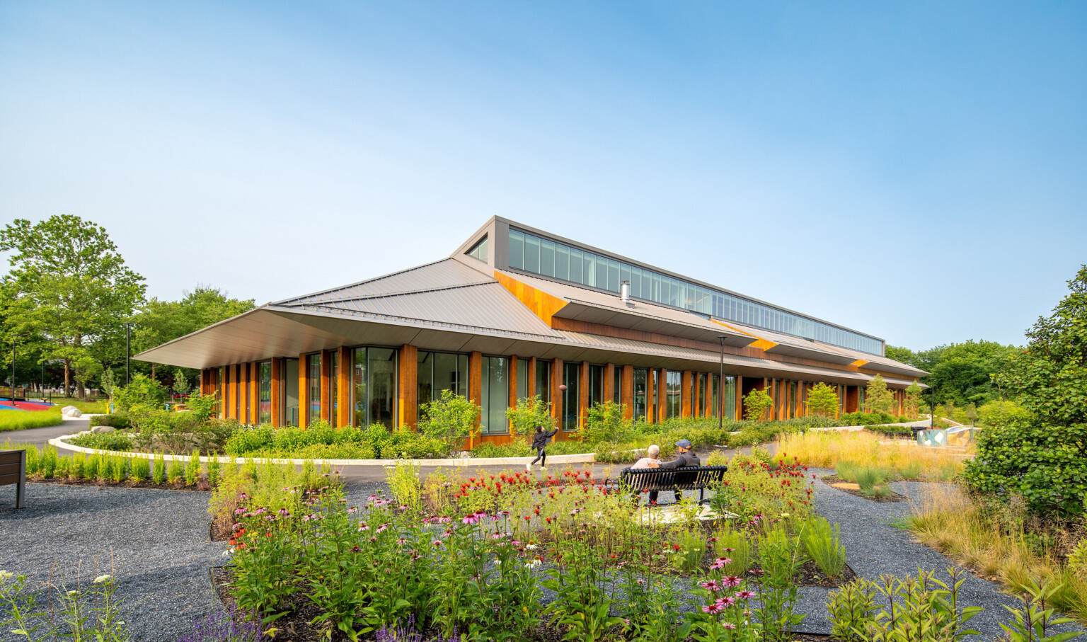 Joy Evans Therapeutic recreation center building; exterior photo with lots of greenspace and pathways to the wood and grey building; pointed roof with large windows