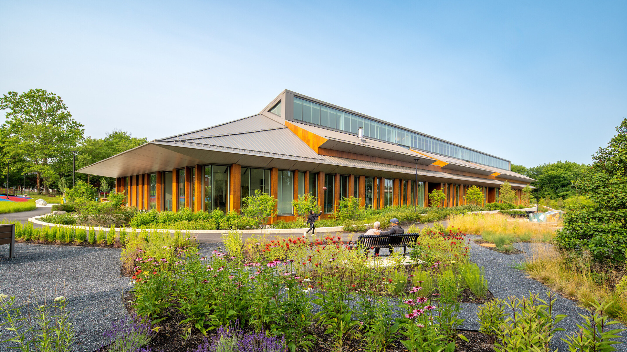 Joy Evans Therapeutic recreation center building; exterior photo with lots of greenspace and pathways to the wood and grey building; pointed roof with large windows