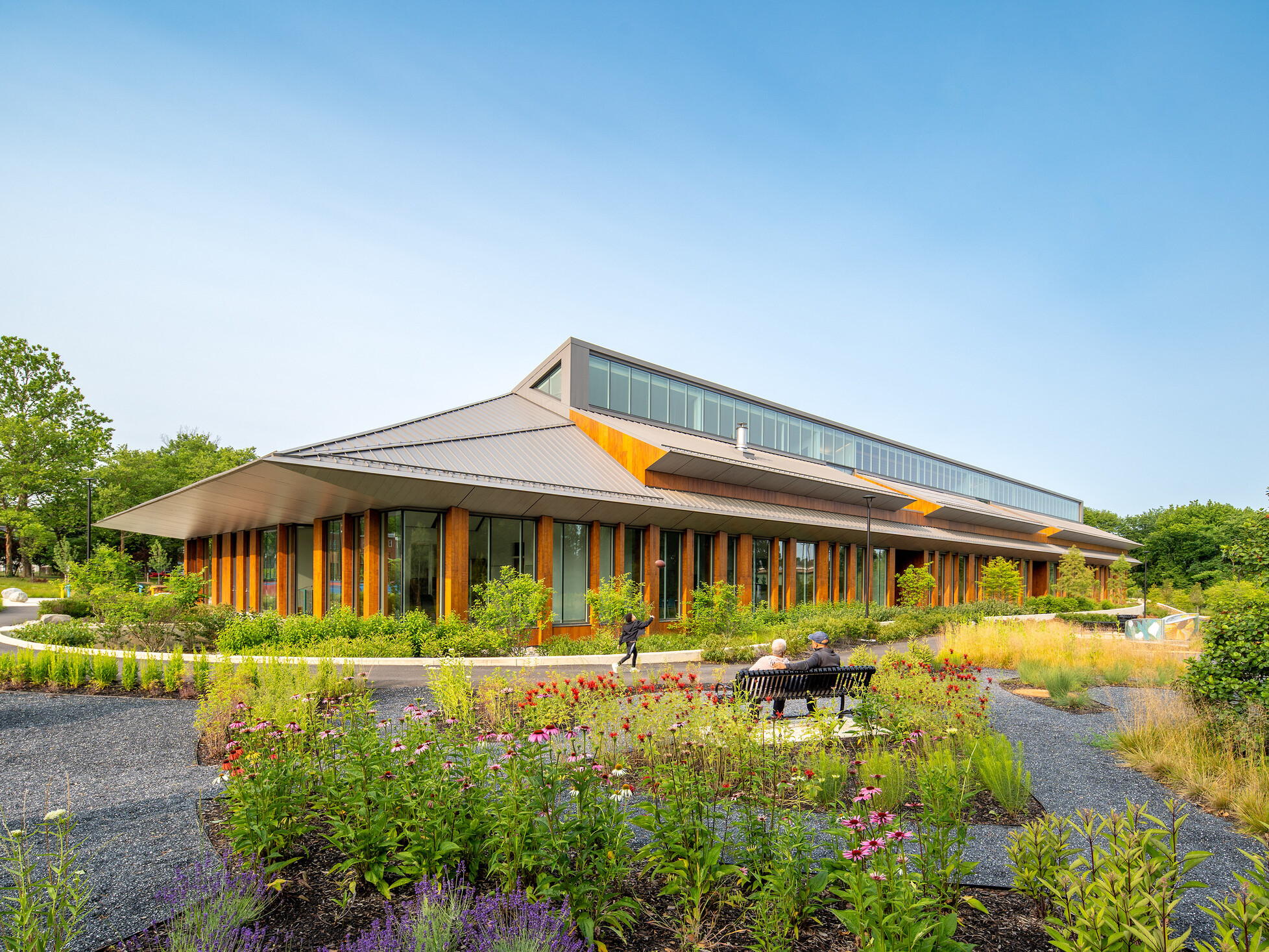 Joy Evans Therapeutic recreation center building; exterior photo with lots of greenspace and pathways to the wood and grey building; pointed roof with large windows
