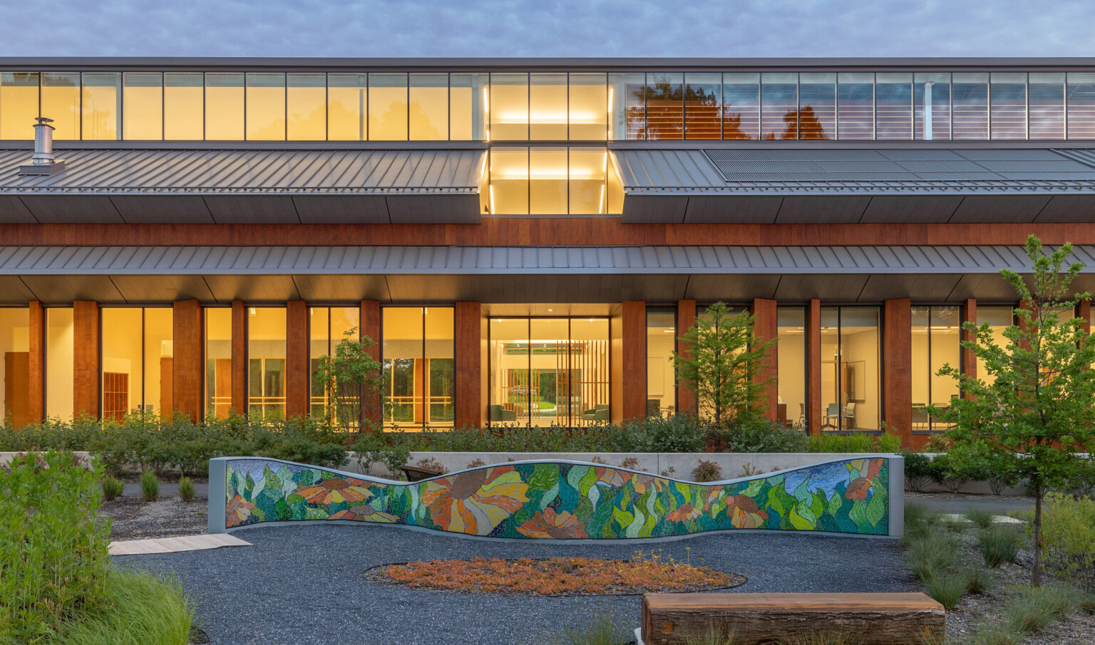 front entrance to Joy Evans Recreation Center; mass timber building with floor to ceiling windows and a gray slanted roof; stone walkways and greenspace in the foreground