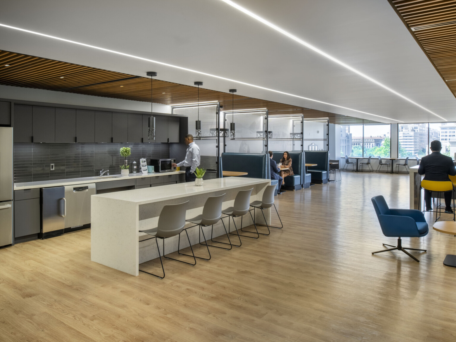 Modern office kitchen and lounge with multiple seating areas and large windows