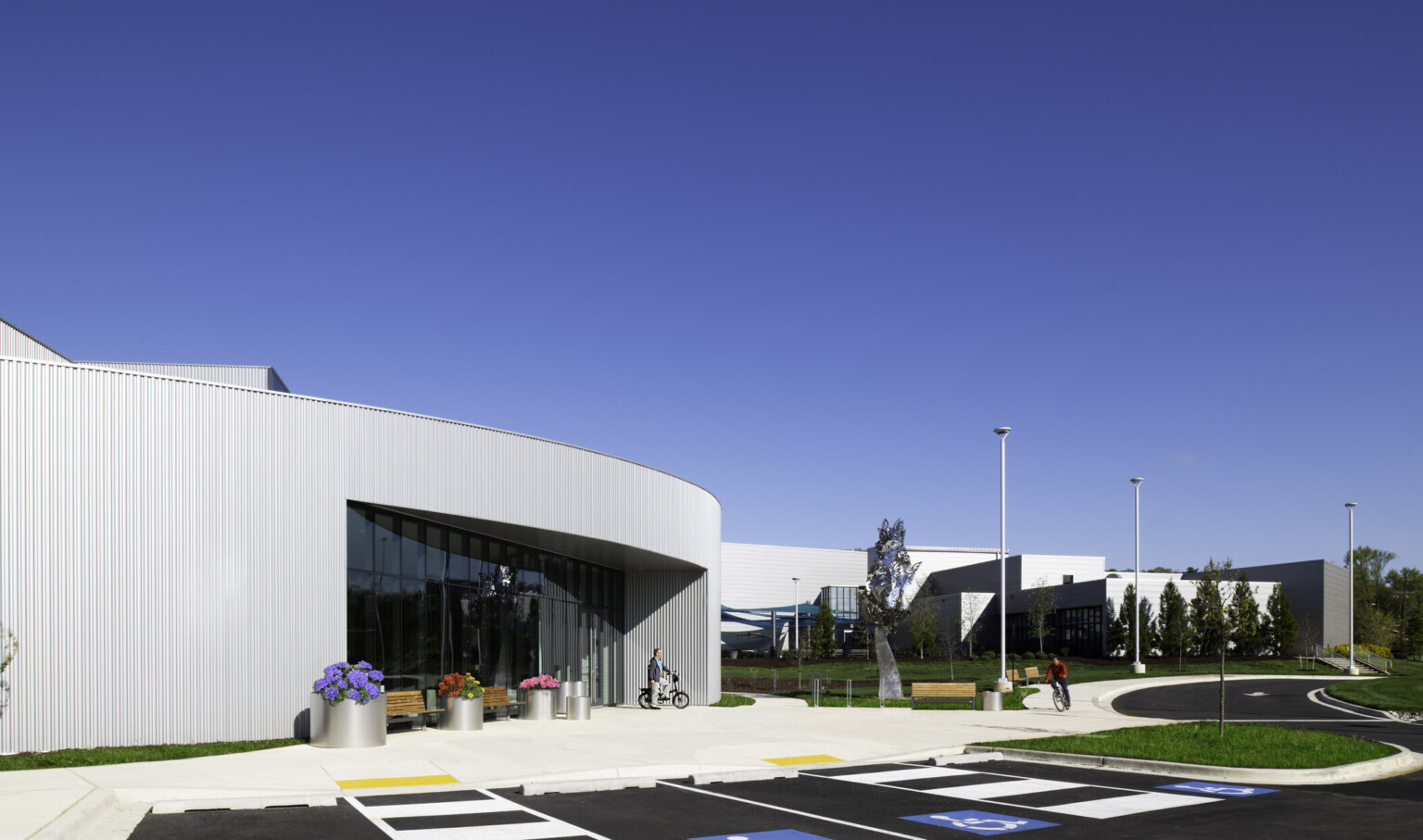 Modern building with glass windows, a bicycle, and colorful flowers under a clear blue sky.