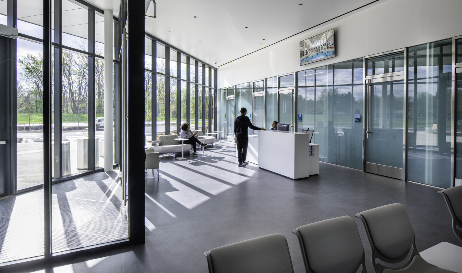 Modern, light-filled room with floor-to-ceiling windows, a reception desk, and seating area.