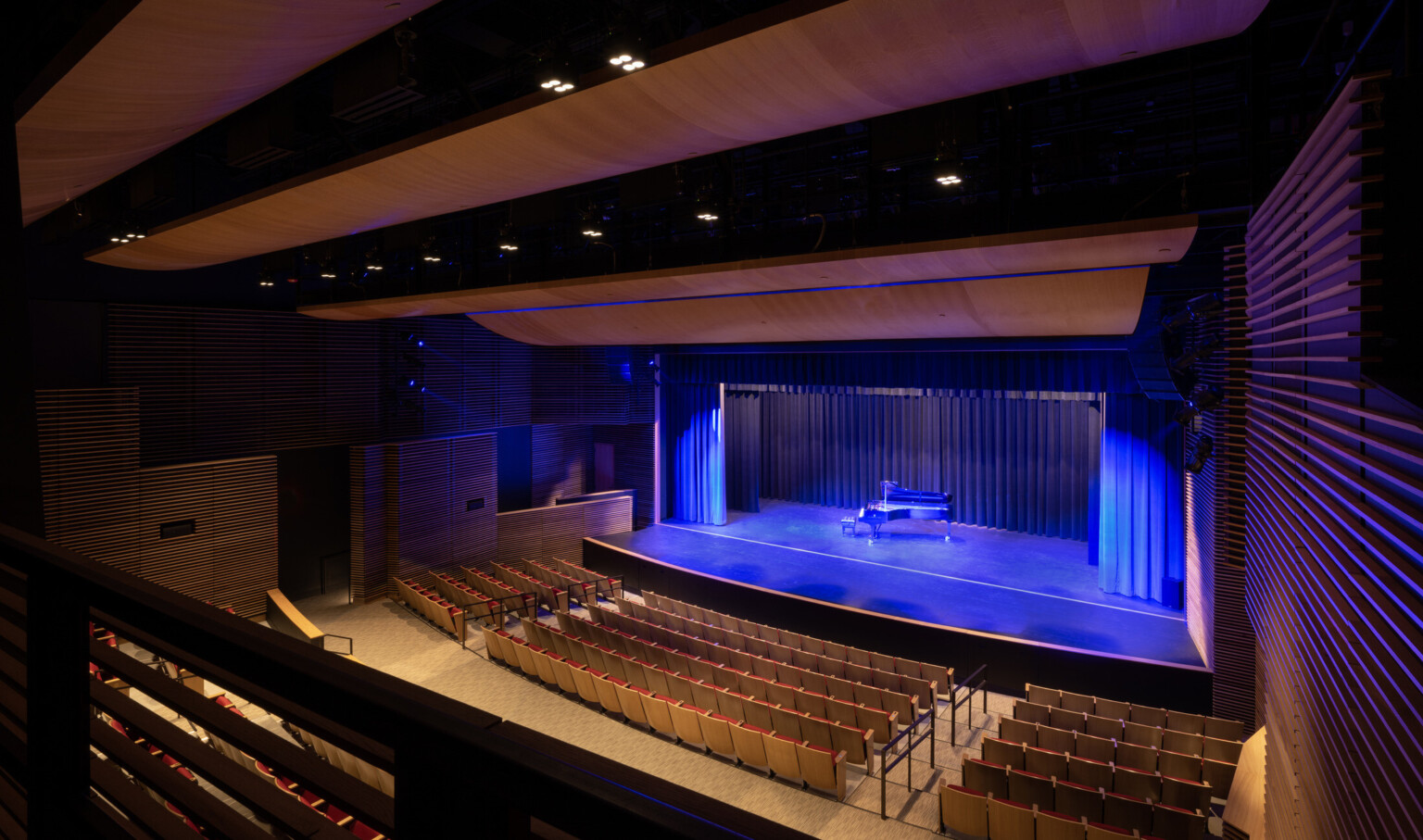 A theater stage with a grand piano and blue lighting, set against a backdrop of red seats in a dimly lit auditorium.