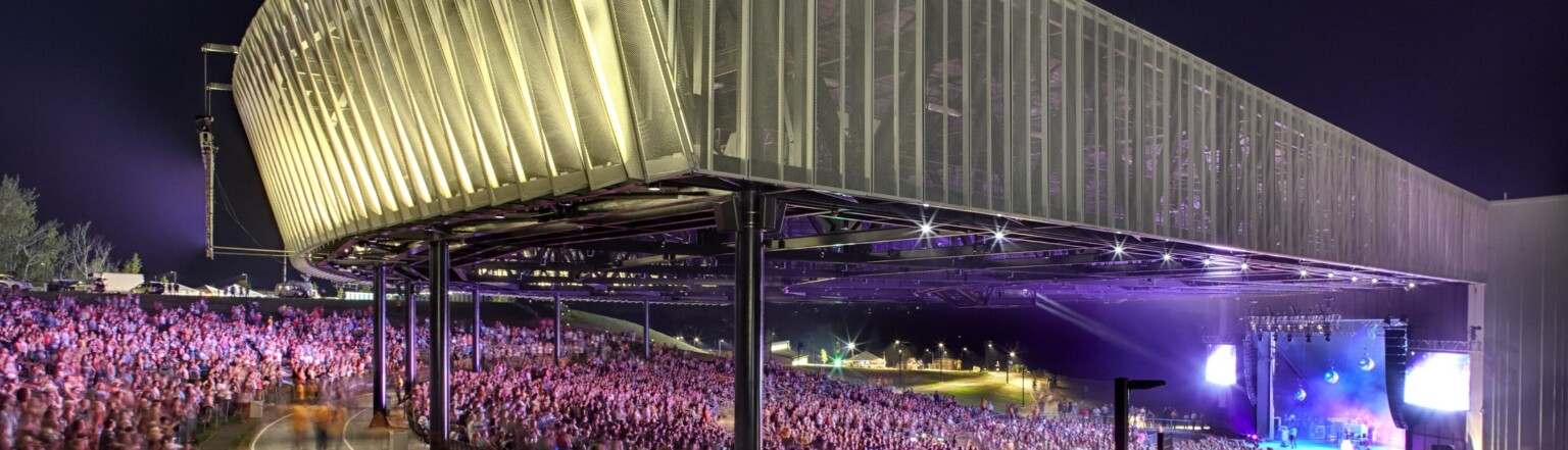 Corner view of crowd in partially covered St. Joseph Health Amphitheater at Lakeview at night while band performers on stage