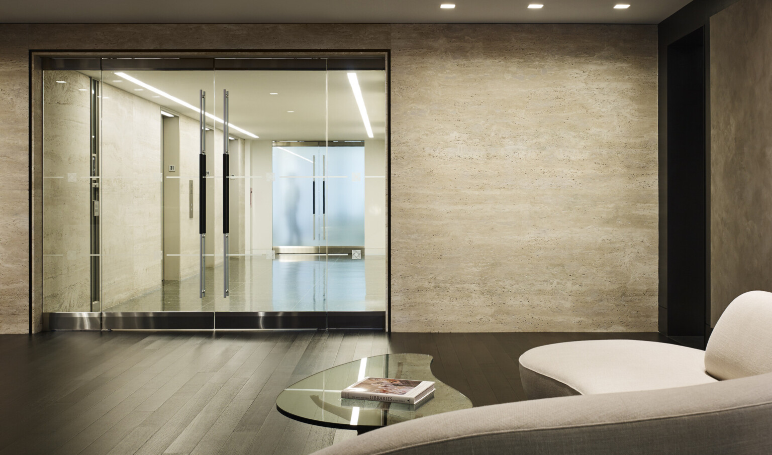 Seating and coffee table in front on glass double doors looking to elevator hallway with light colored walls
