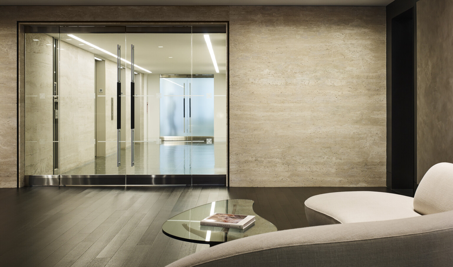 Seating and coffee table in front on glass double doors looking to elevator hallway with light colored walls