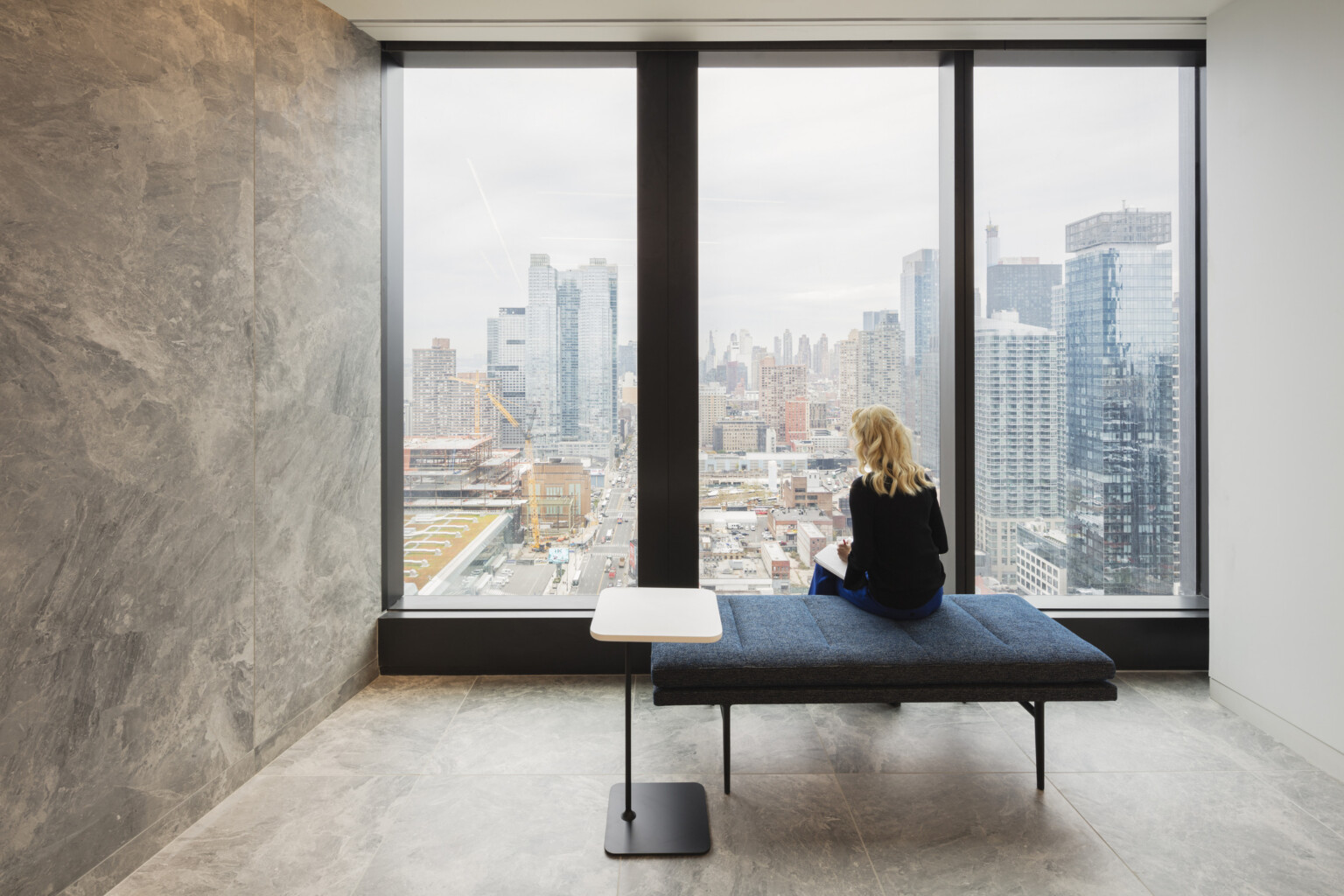 woman sitting in front of a floor to ceiling window overlooking cityscape