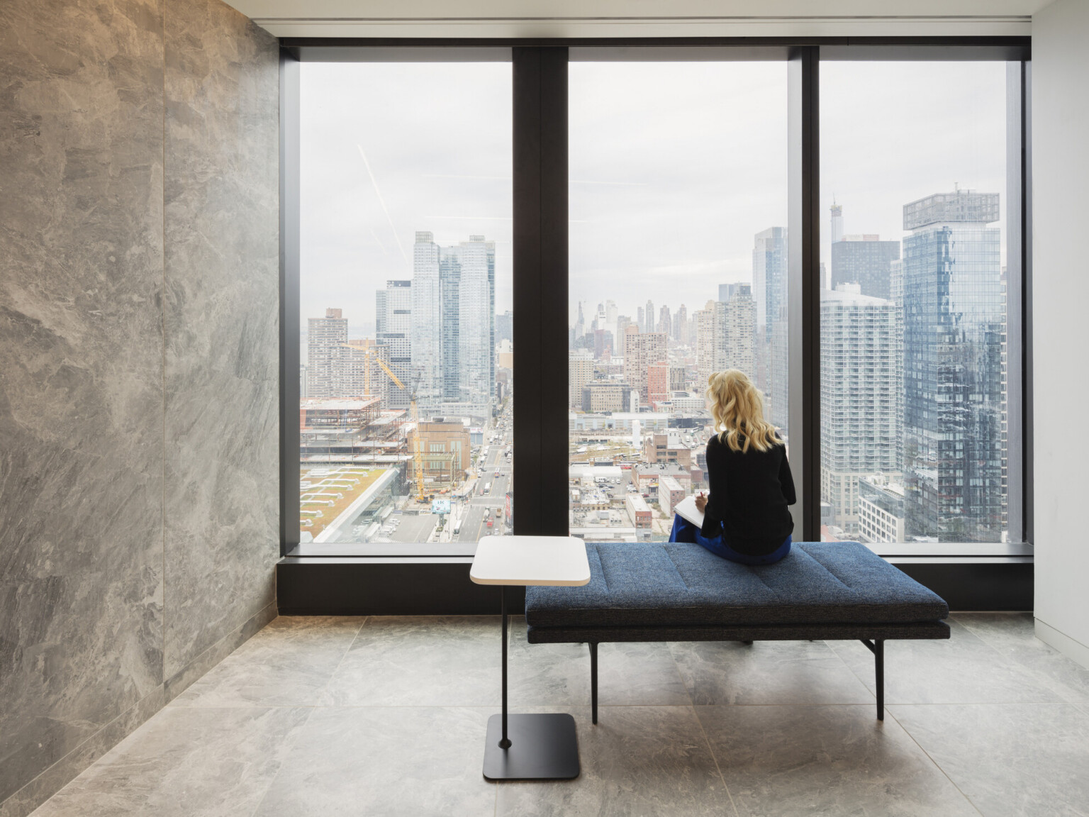 woman sitting in front of a floor to ceiling window overlooking cityscape