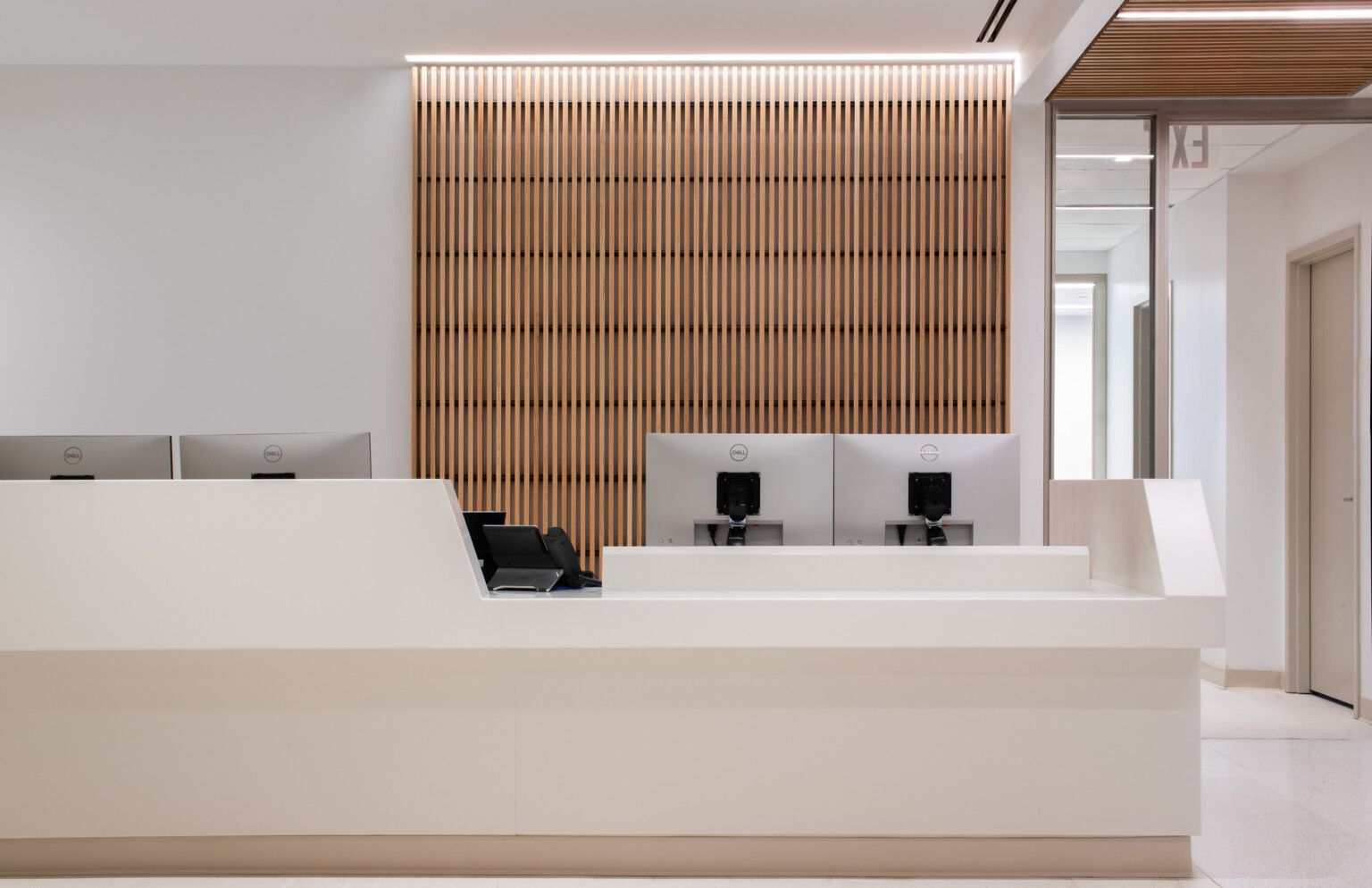 View of a medical office waiting room with a wooden backdrop with computers on a desk and chairs in the lobby area