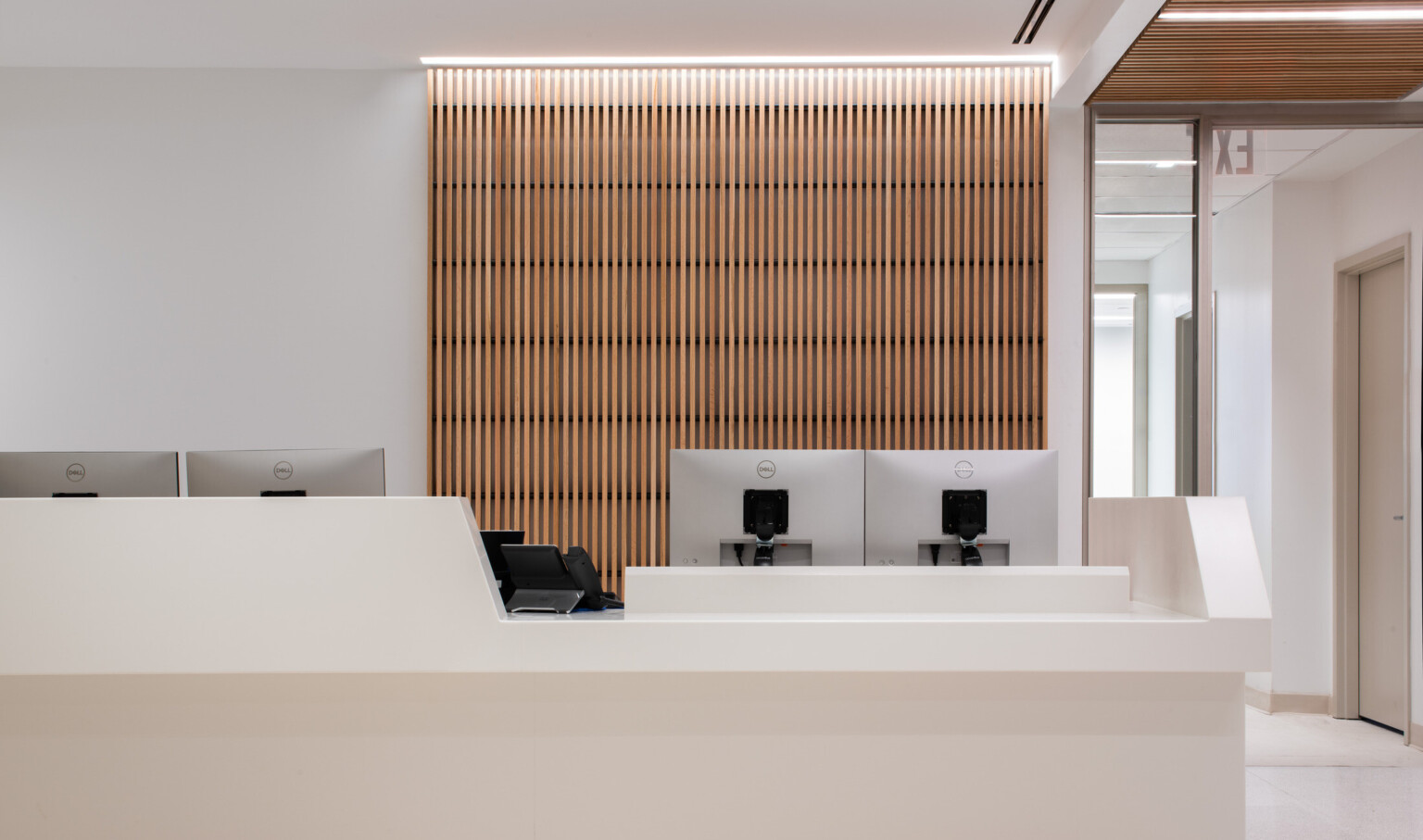 View of a medical office waiting room with a wooden backdrop with computers on a desk and chairs in the lobby area