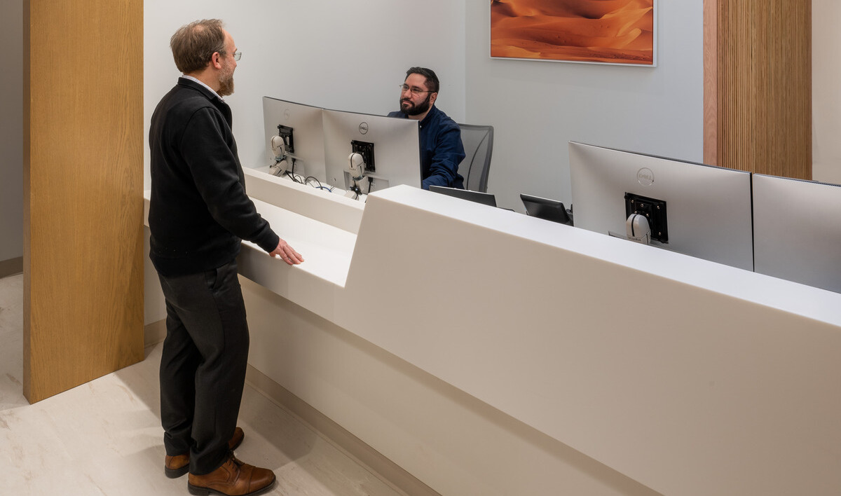 Man speaking to another gentleman in an office setting with computers, white walls, and wooden accents