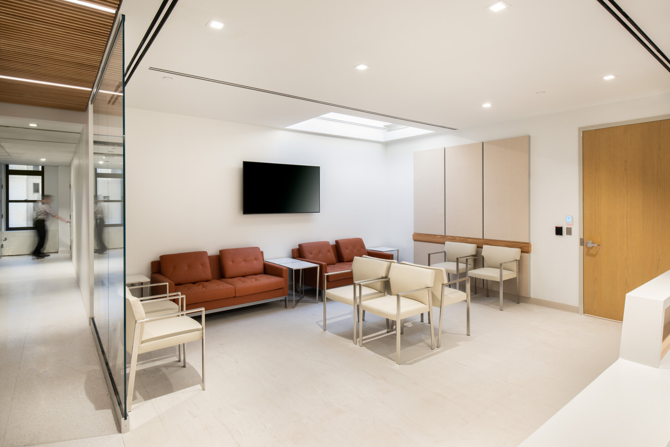 Hospital waiting room filled with modern ivory and terracotta furniture, TV hanging on the backwall and a view down the hallway to the left