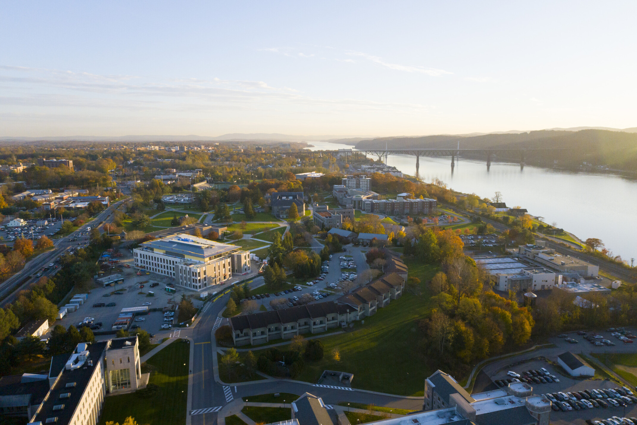 Aerial view of Marist University showing buildings settled in fall colored foliage in front of a river.