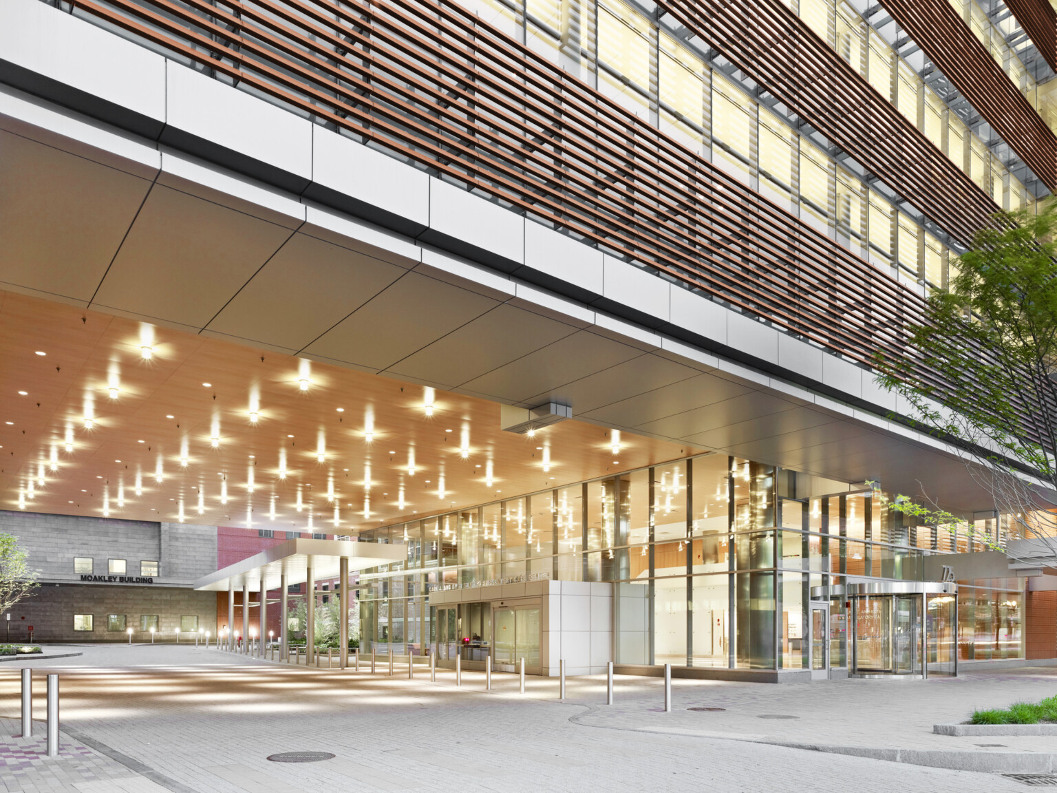 Exterior of building with a large overhang, glass walls, and ceiling lights. Trees and plants surround the clean, contemporary structure.