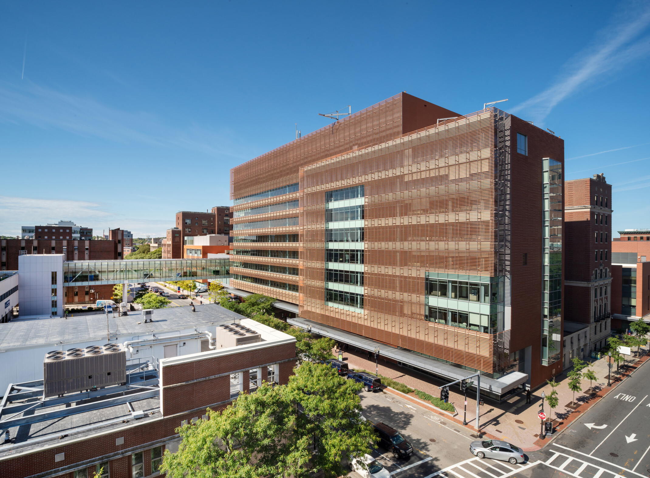 A large, modern building with a brick façade and numerous windows stands in an urban area. Other buildings are visible in the background.