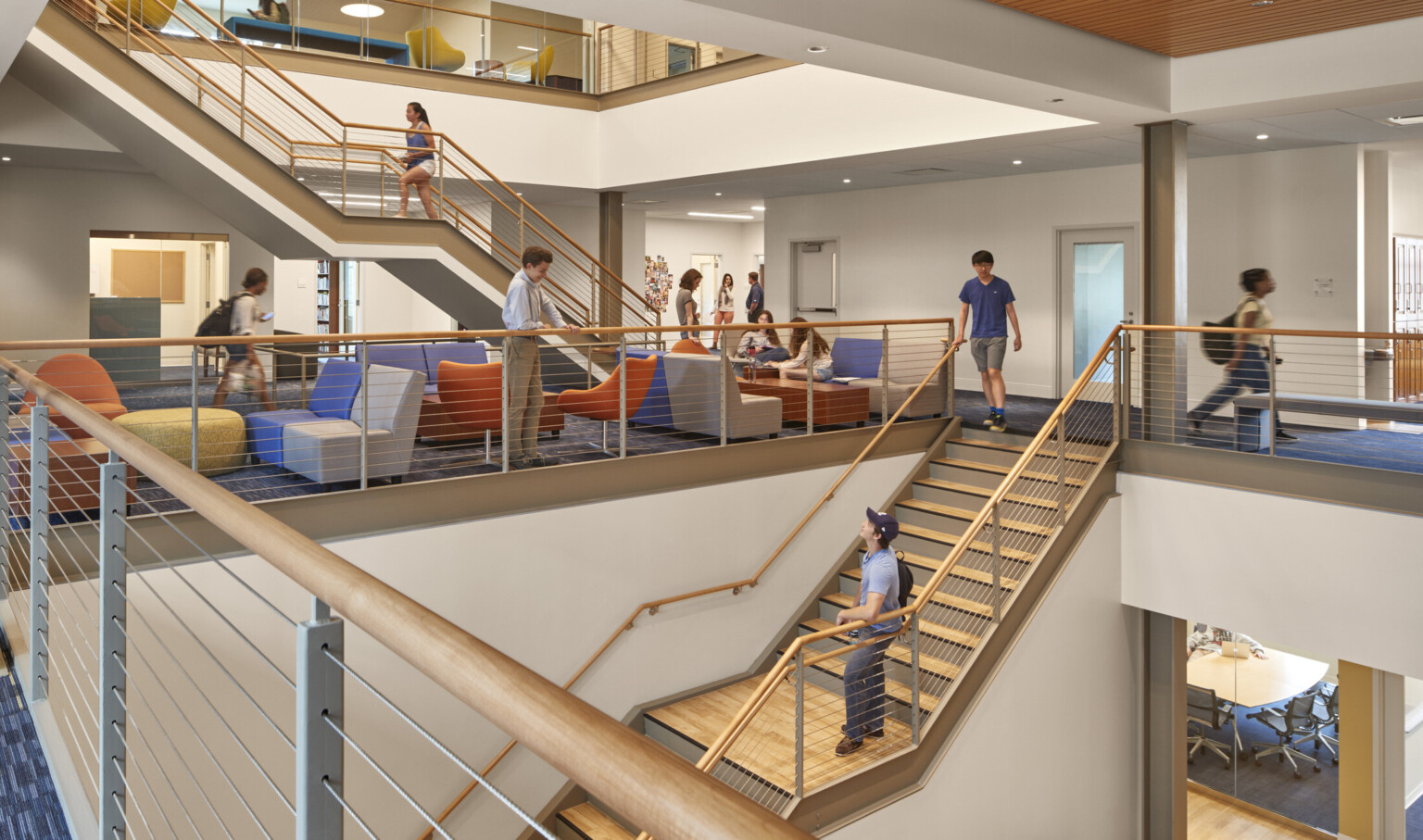 2nd floor mid level of triple height atrium with wood panel ceiling accents, connecting stairs to left and comfortable seating areas