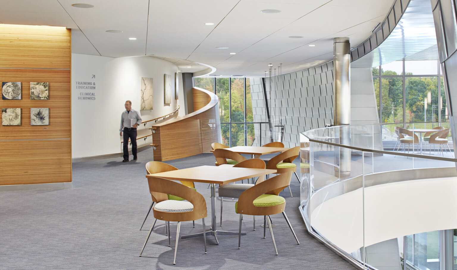 upper lobby area with light wood accents, tables and chairs, and full glass walls with views out to the forest