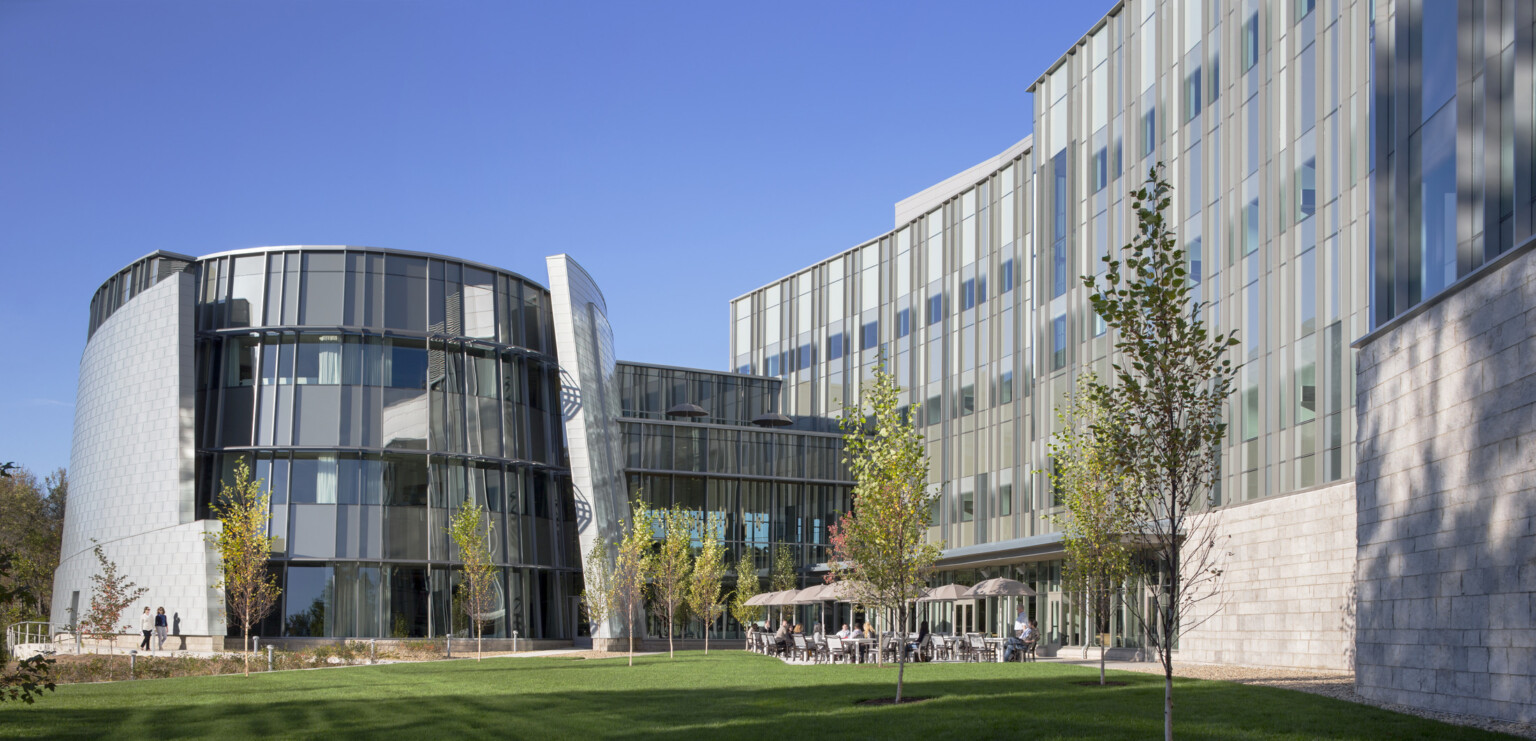 exterior of a world renowend genomic medical center in Connecticut; round glass from anchors one end of the building with an outdoor patio beneath facade with glass fenestration